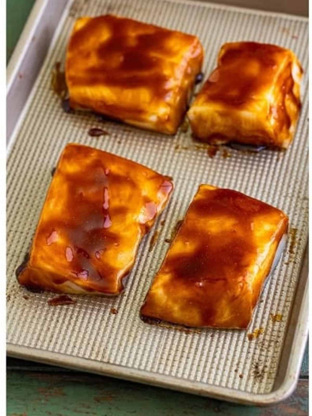Chilean sea bass filets brushed all over with the hoisin soy glaze on a sheet tray.