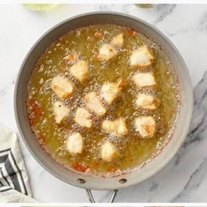 Battered Chinese Chicken bites frying in hot bubbling oil in a large silver skillet, cooking until golden and crispy on the outside, overhead view on marble.
