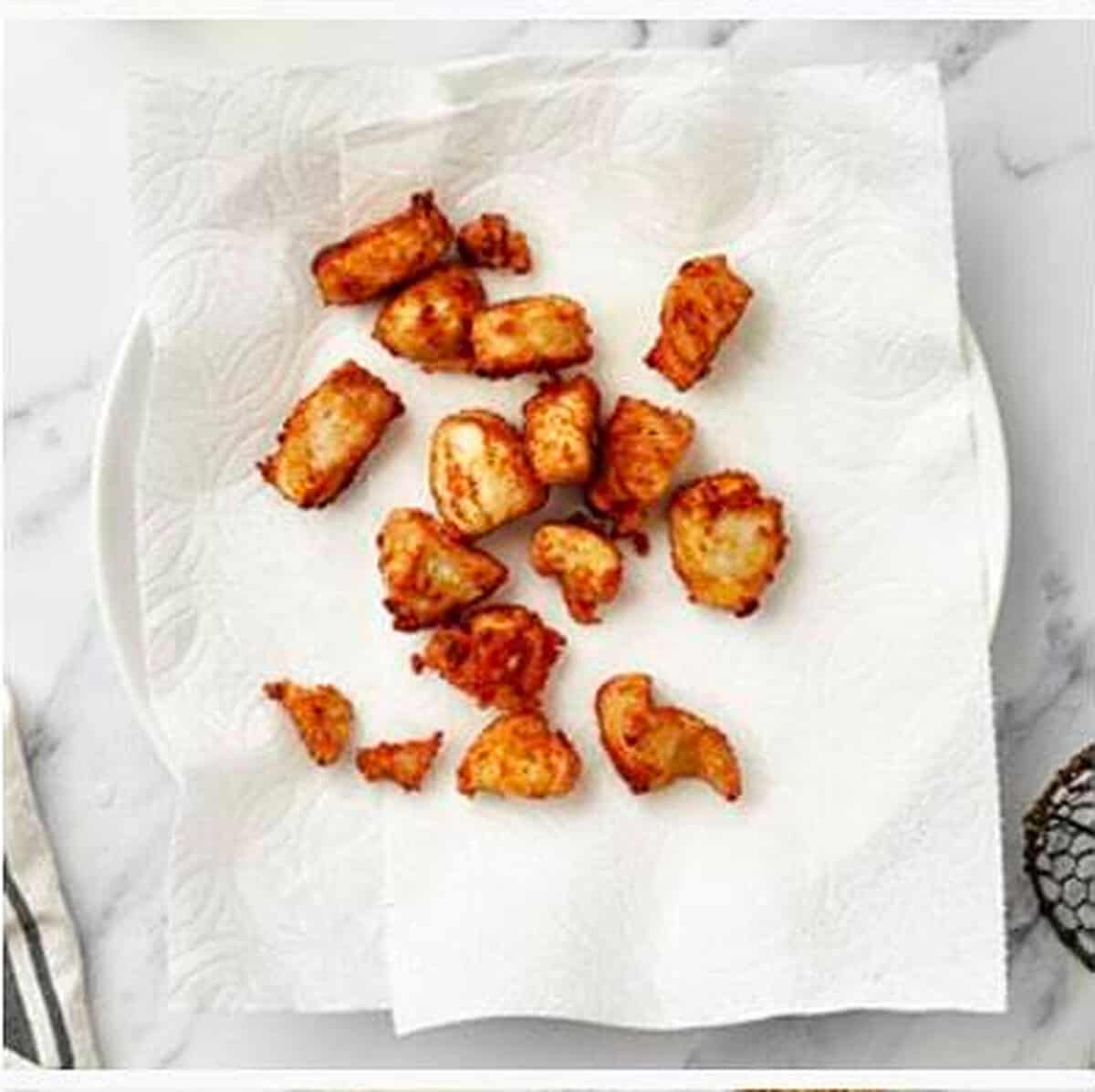 Golden crispy fried Chinese Chicken bites draining on white paper towels on a plate after being removed from hot oil, overhead view on marble surface.