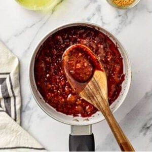 Thick deep red brown sugar soy garlic glaze being stirred with a wooden spoon in a saucepan, cooked down to a rich sticky caramelized consistency.