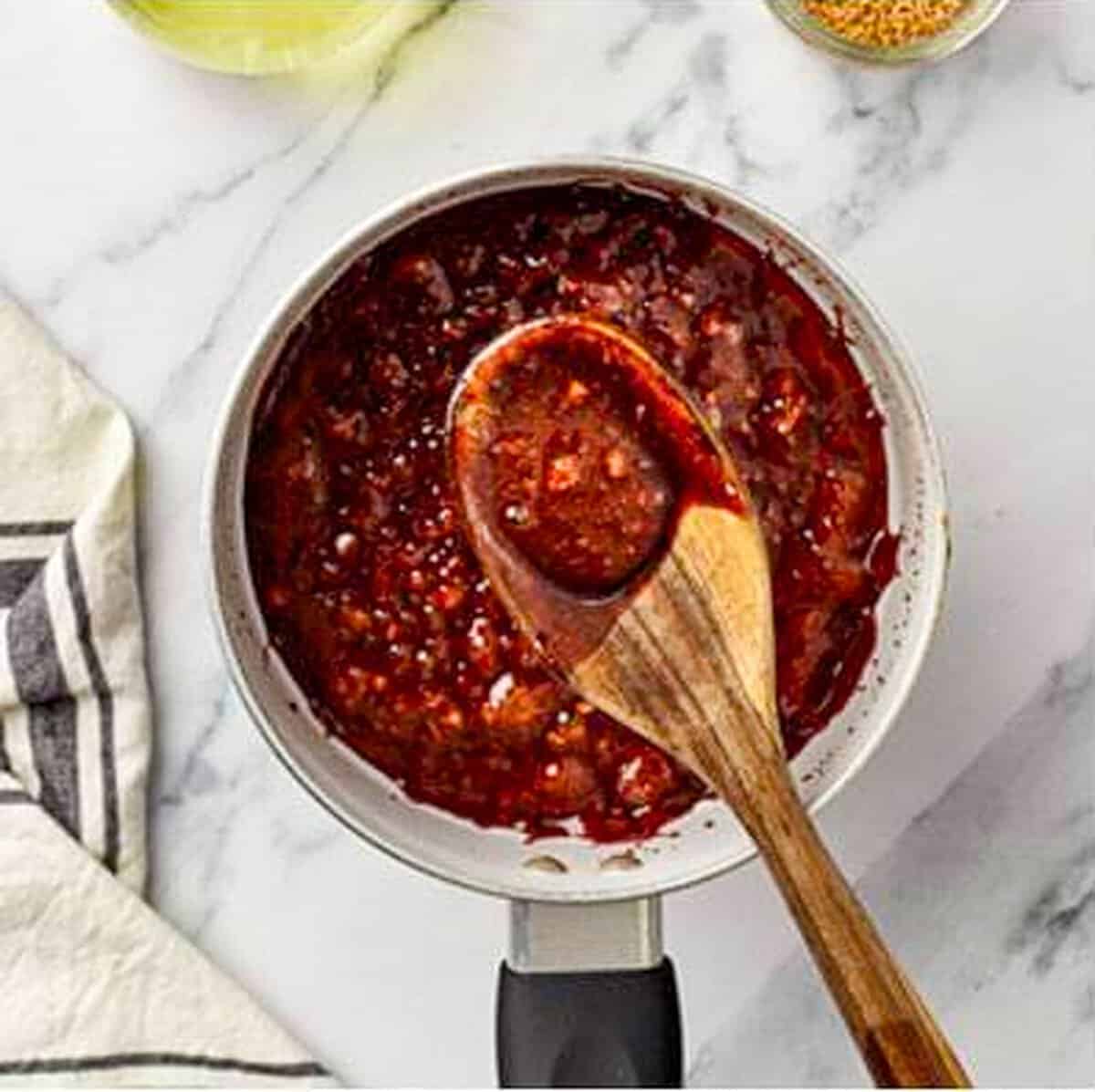 Thick deep red brown sugar soy garlic glaze being stirred with a wooden spoon in a saucepan, cooked down to a rich sticky caramelized consistency.