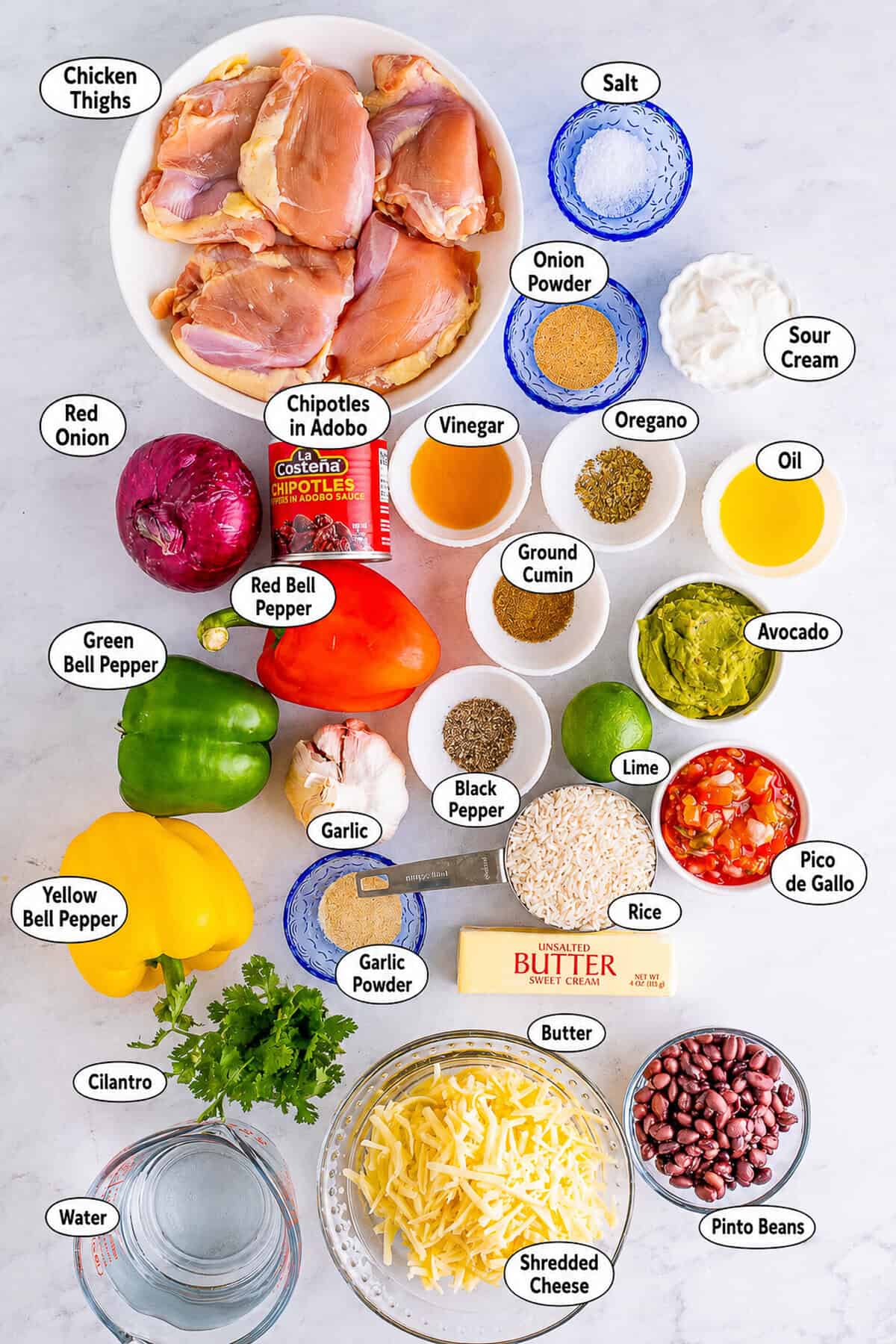 Fresh ingredients for a Chipotle Bowl Recipe arranged on the counter including chicken thighs, rice, black beans, bell peppers, and pico de gallo.