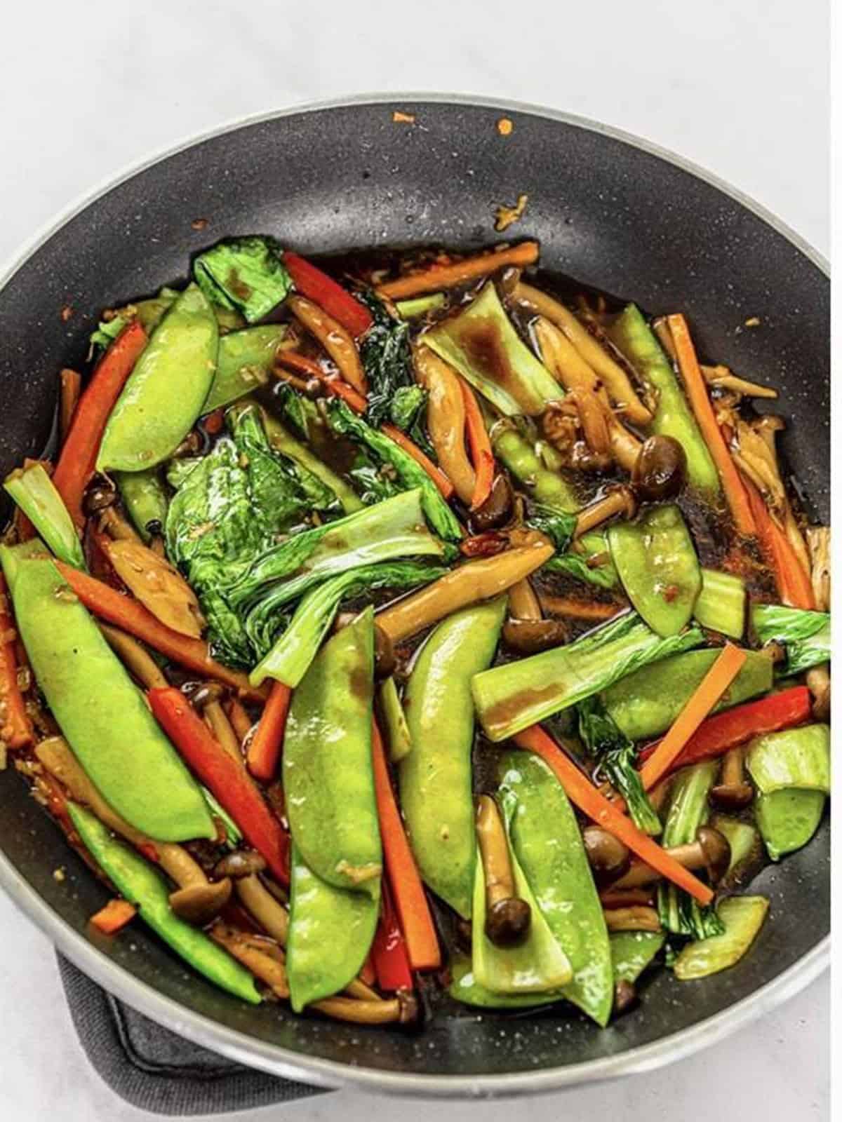 Bok choy, snow peas, carrots, and bell peppers stir fried in the wok with sauce.