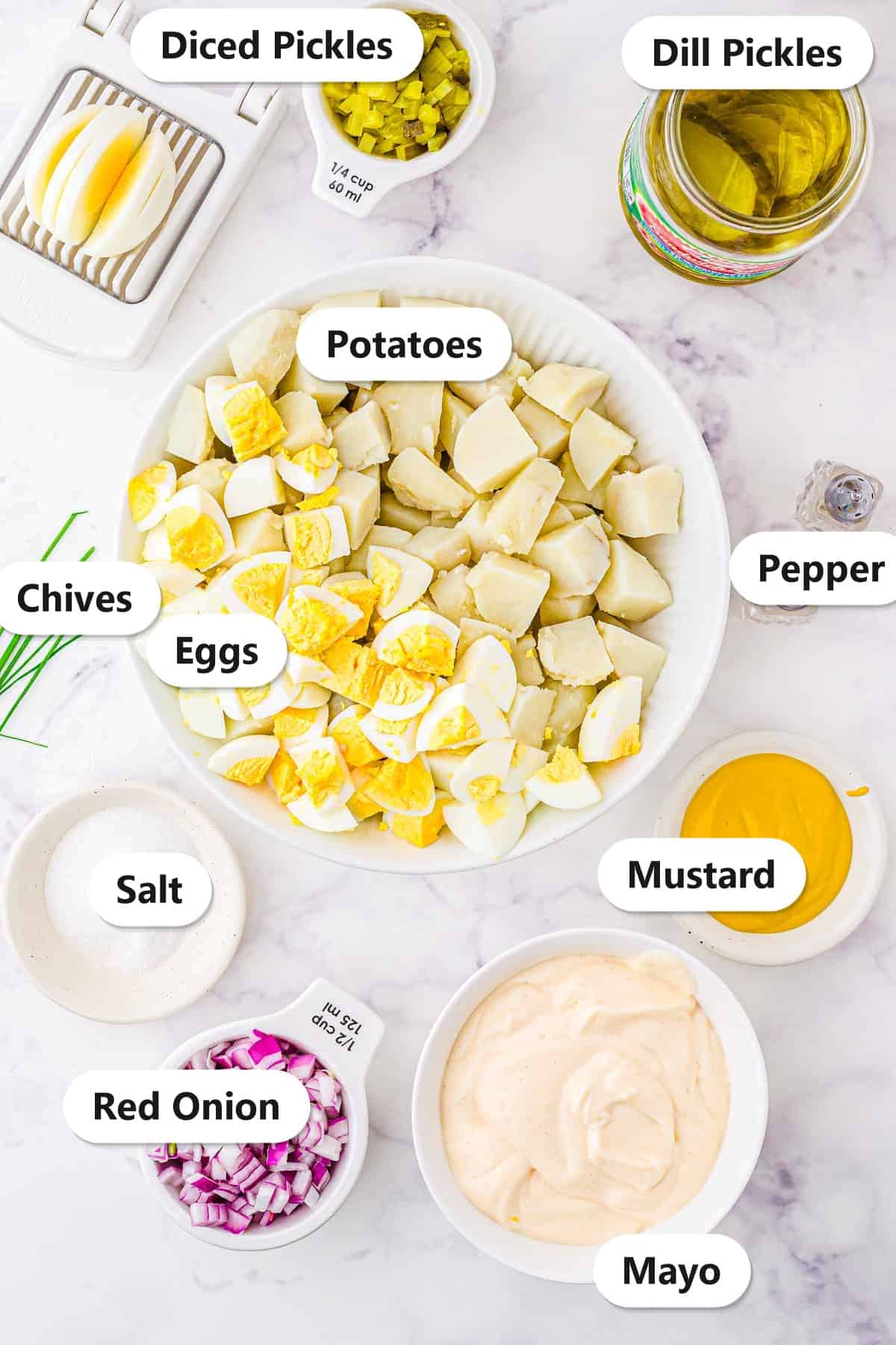 Labeled raw ingredients for Classic Potato Salad including diced pickles, dill pickles, potatoes, eggs, chives, pepper, salt, mustard, red onion, and mayo.