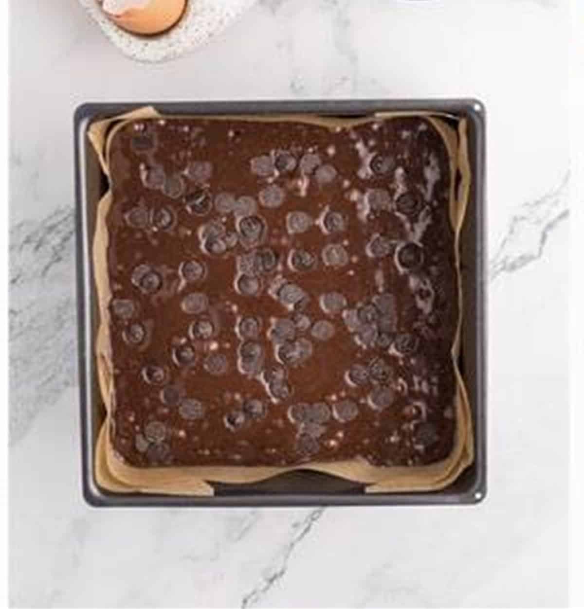 Brownie batter poured into a lined pan and topped with chocolate chips.