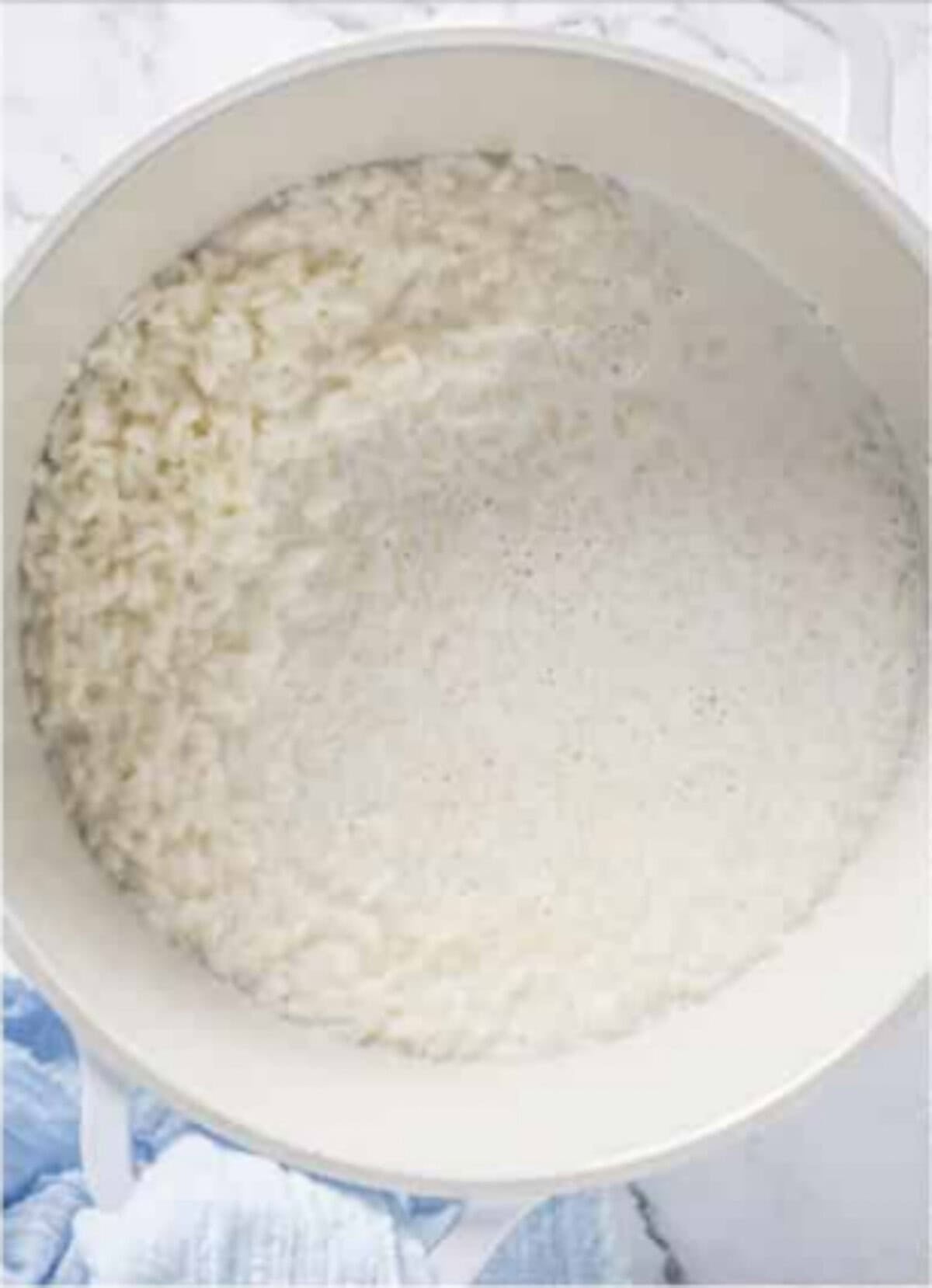 Cooked white rice and milk in a small saucepan starting Rice Pudding Recipe on the stovetop.