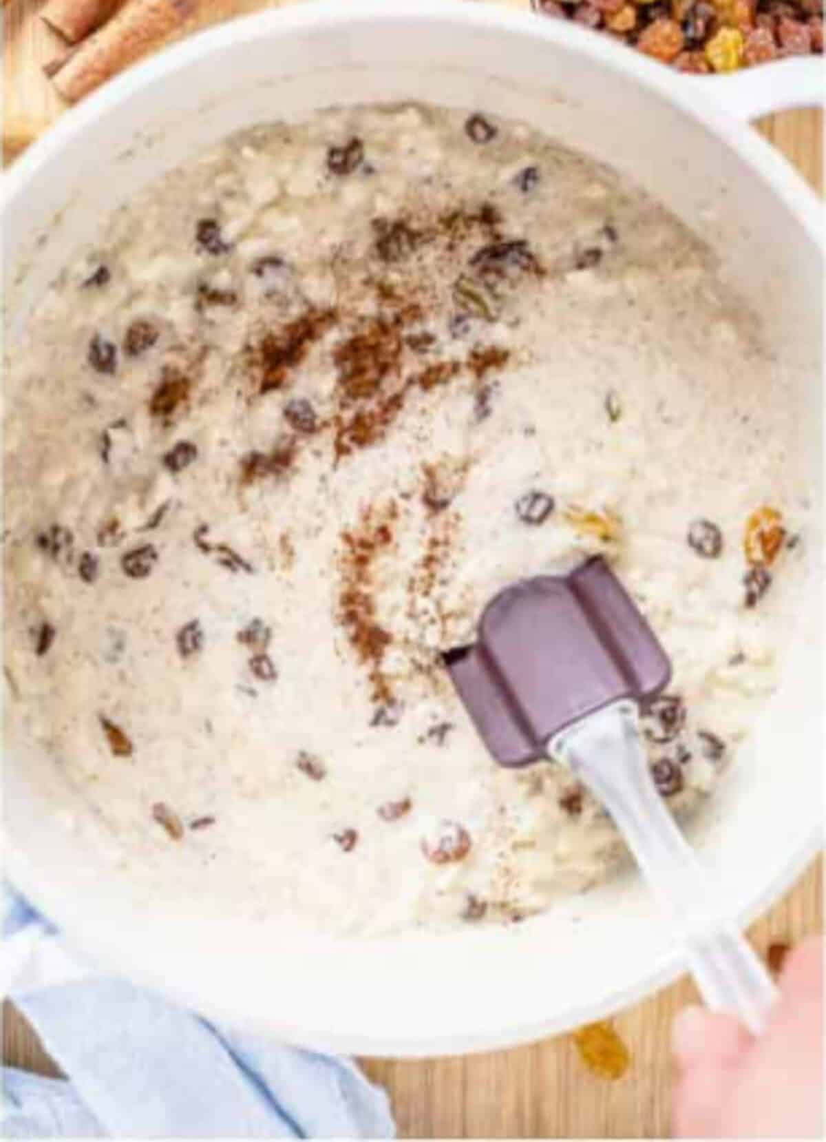 Finished Rice Pudding Recipe with raisins, cinnamon dust on top, and a spatula stirring in vanilla and butter.