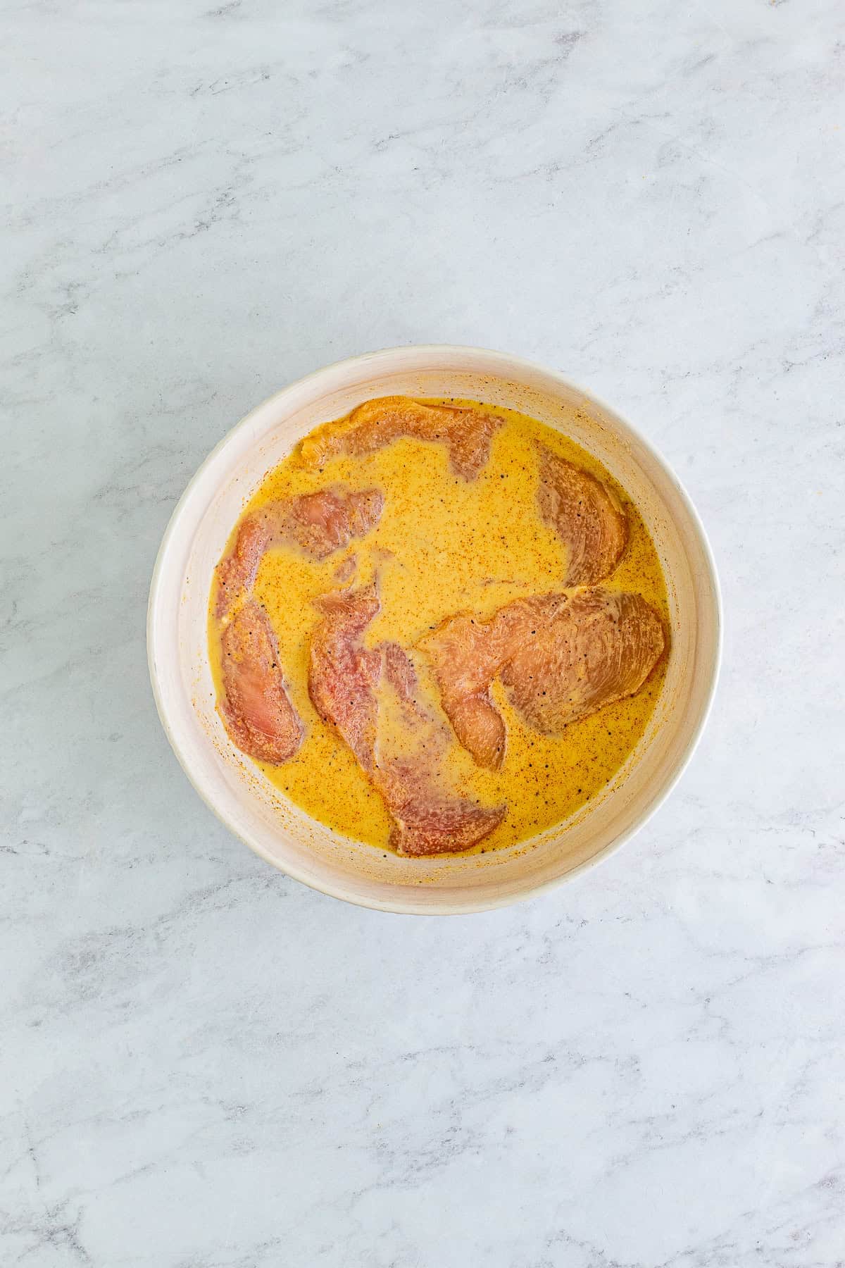 Chicken breasts marinating in pickle juice and seasonings in a bowl.