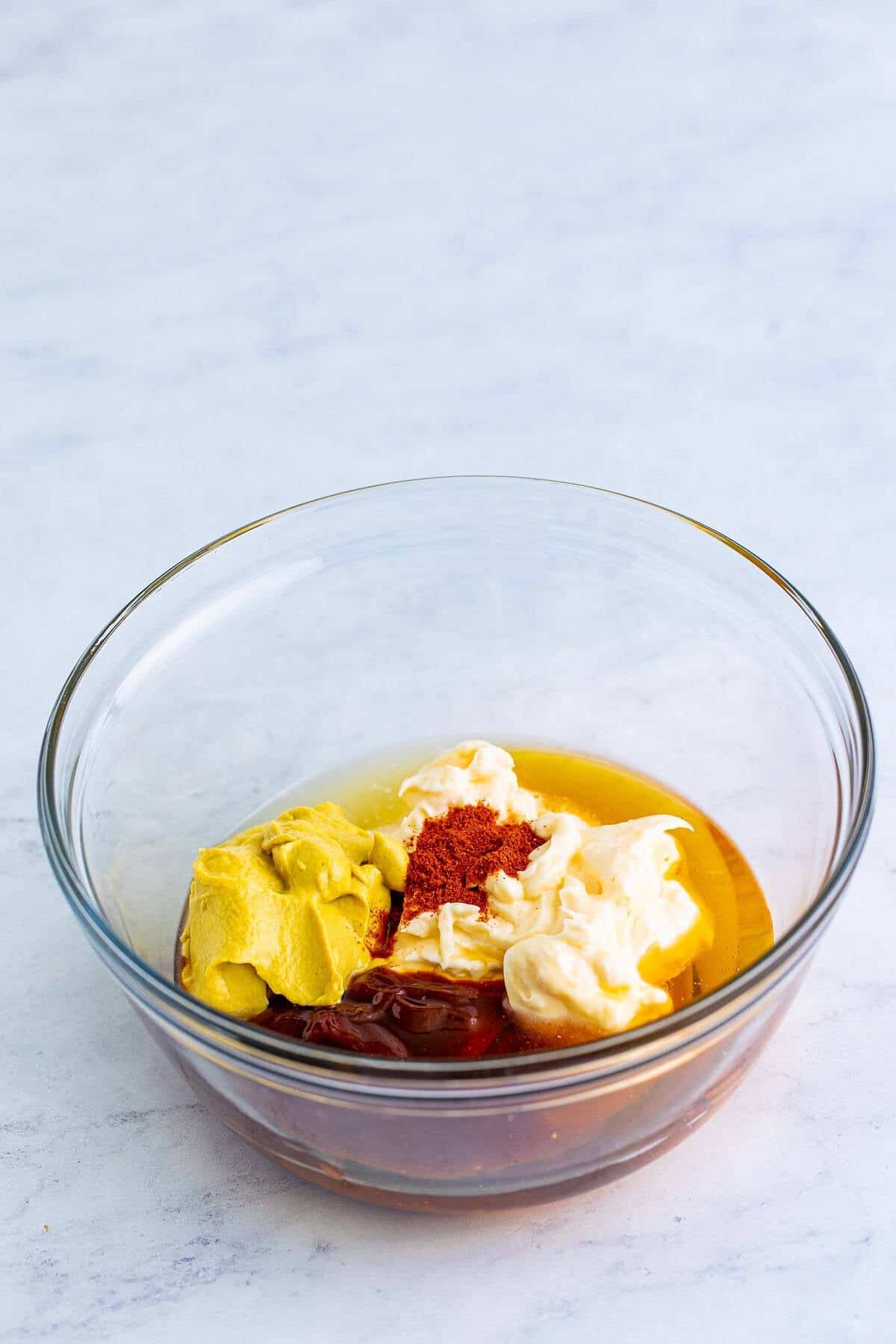 Mayonnaise, sweet bbq sauce, honey, dijon mustard, lemon juice, and smoked paprika being whisked together in a medium glass bowl to make the Chick-Fil-A Honey Roasted BBQ Sauce Recipe.