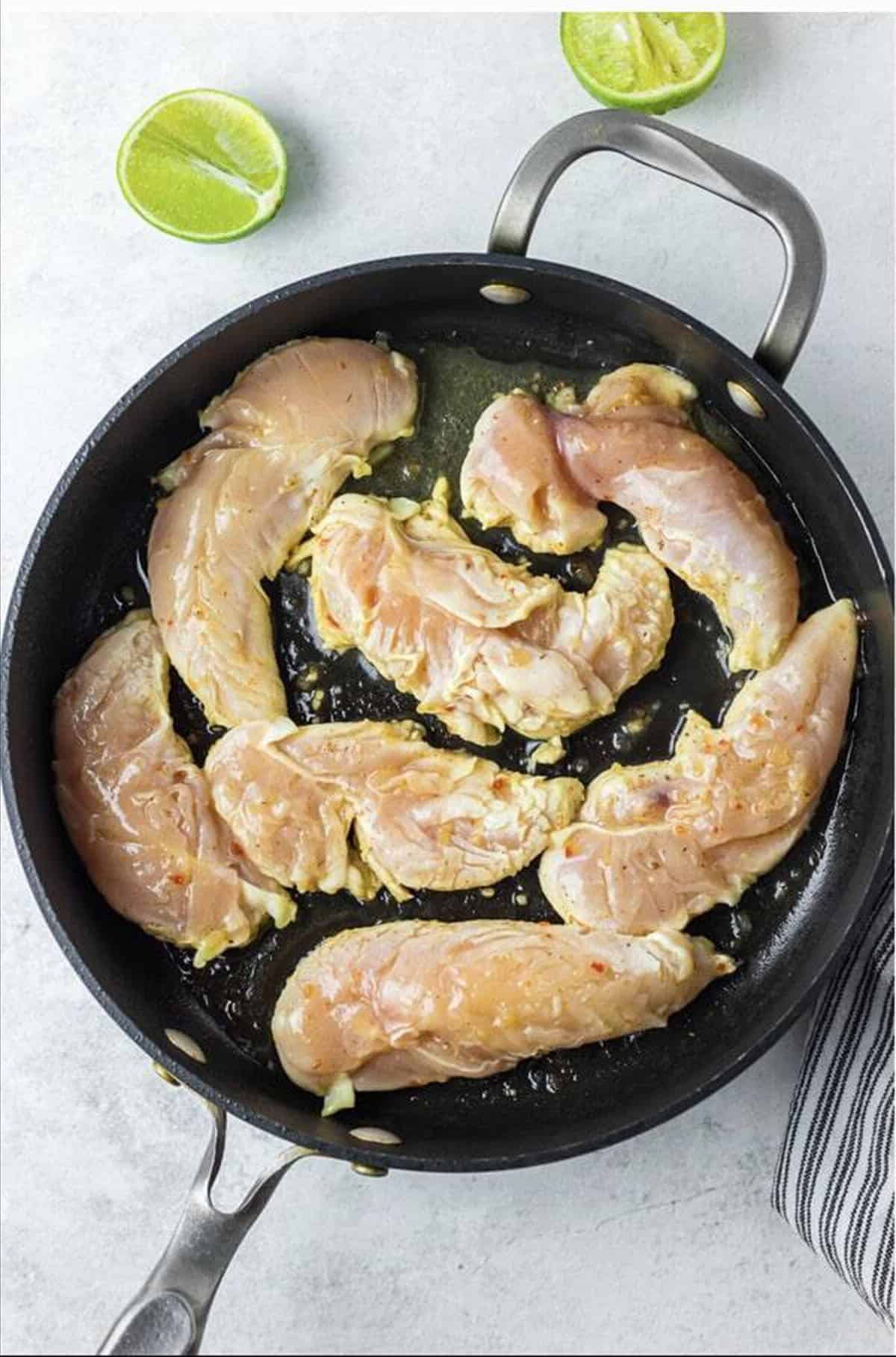 Marinated raw chicken tenderloins arranged in a dark skillet ready to cook for Cracker Barrel Chicken Tenders.