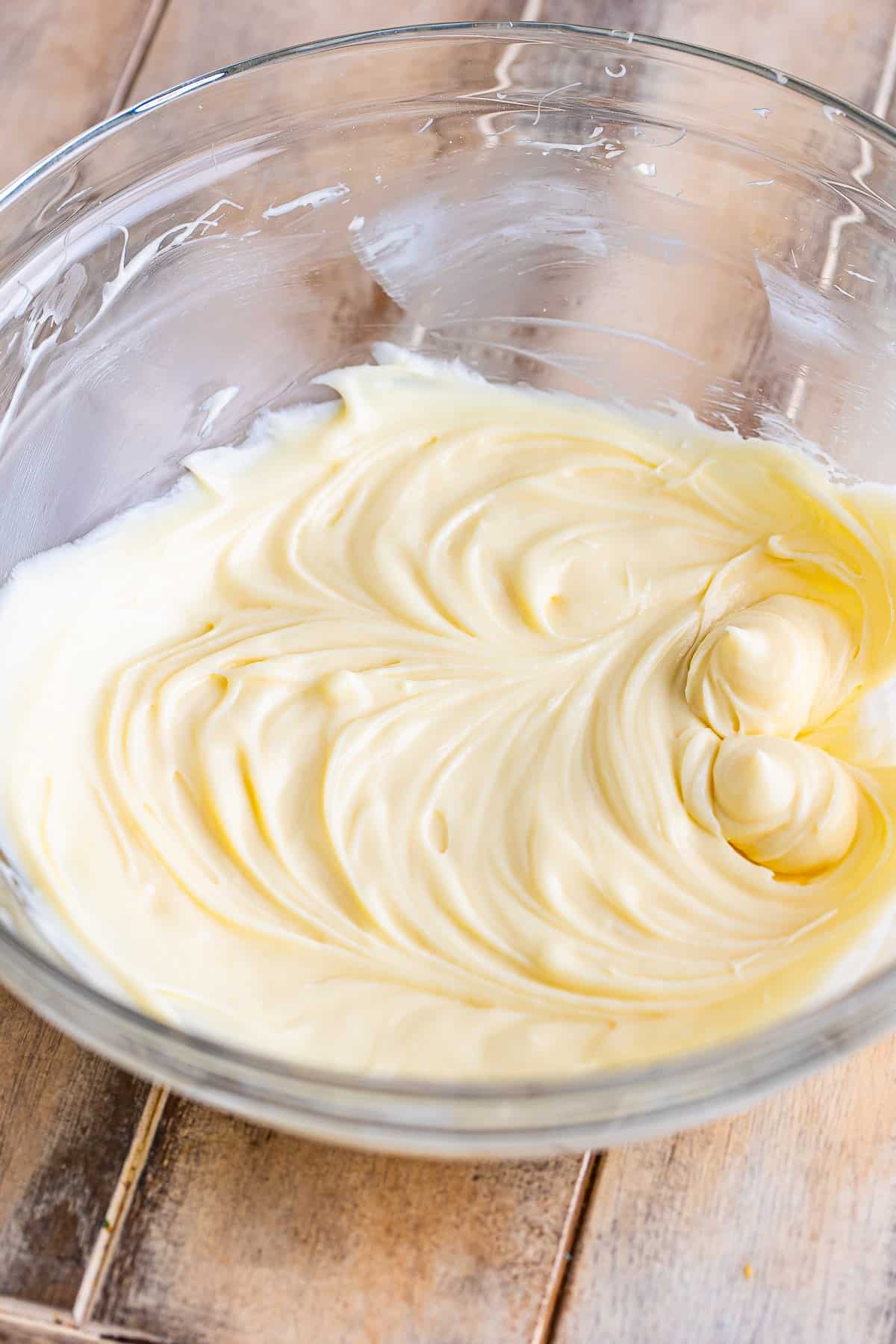 Glass mixing bowl with cream cheese, powdered sugar, and vanilla being whipped together for the Cream Cheese Fruit Dip recipe.