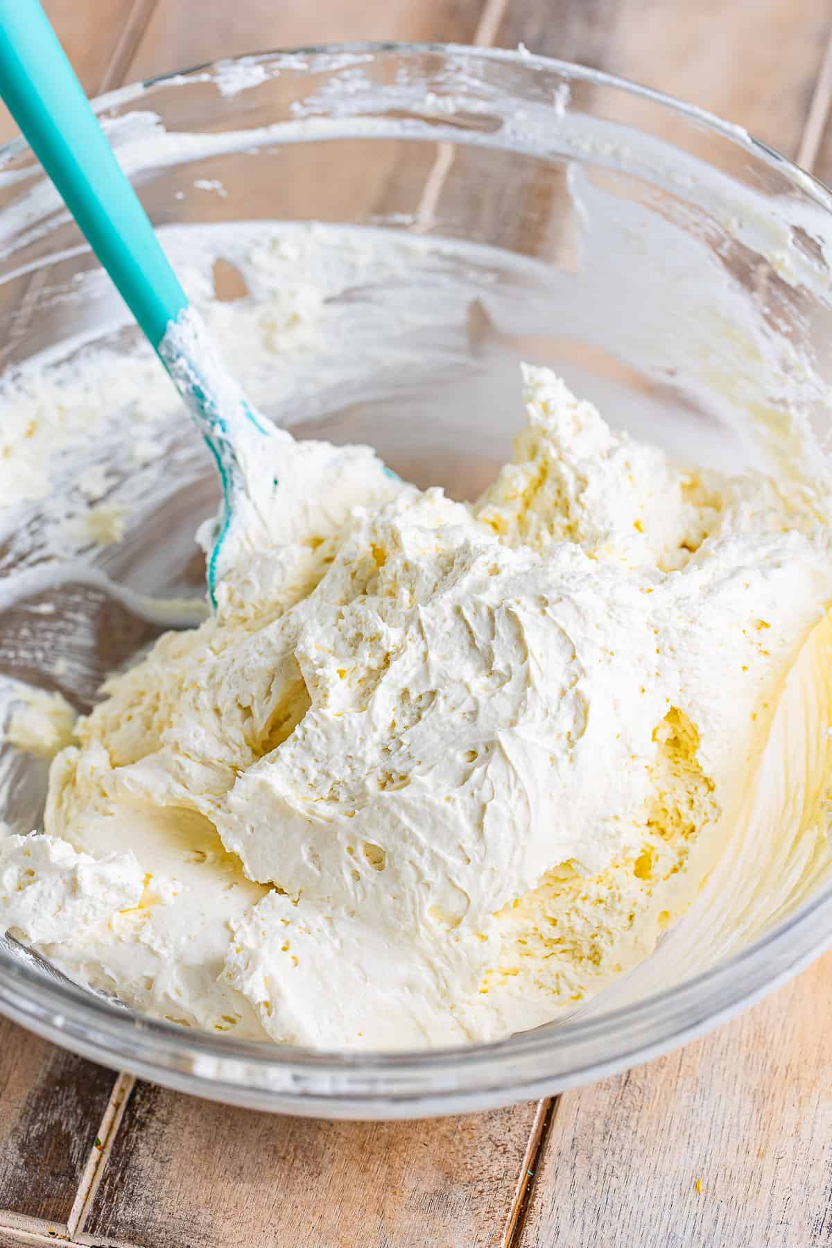 Teal rubber spatula folding Cool Whip into the cream cheese mixture for the Cream Cheese Fruit Dip recipe.