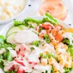 Creamy Garlic Salad Dressing drizzled over a fresh green salad with cucumbers, tomatoes, peppers, and cheese cubes.
