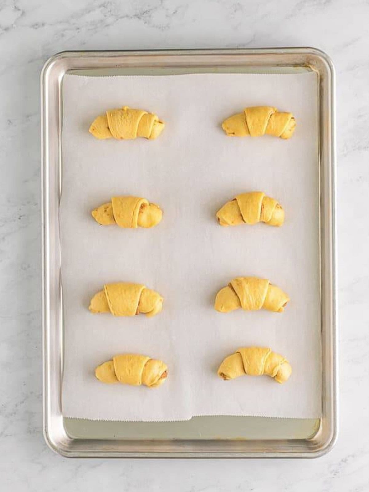Crescent dough rolled up into cinnamon rolls on a parchment lined sheet.