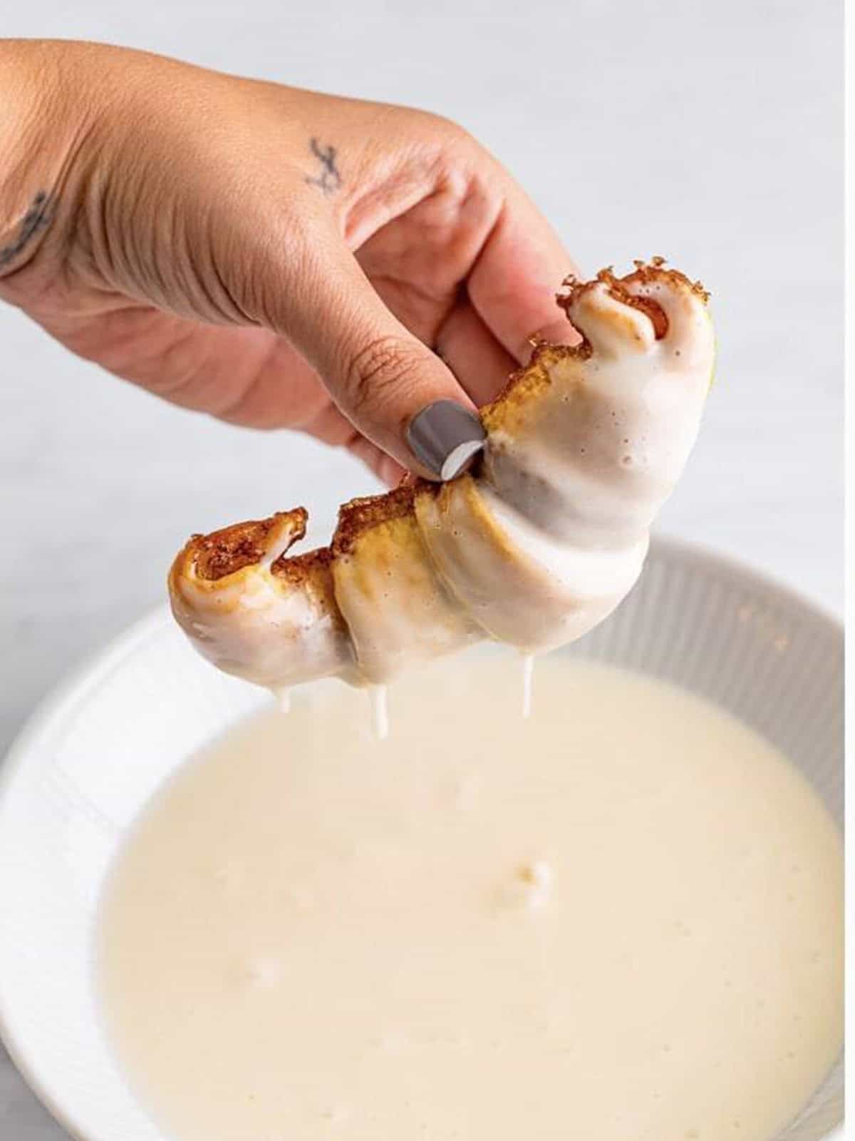 Dipping a baked cinnamon roll into the vanilla glaze.