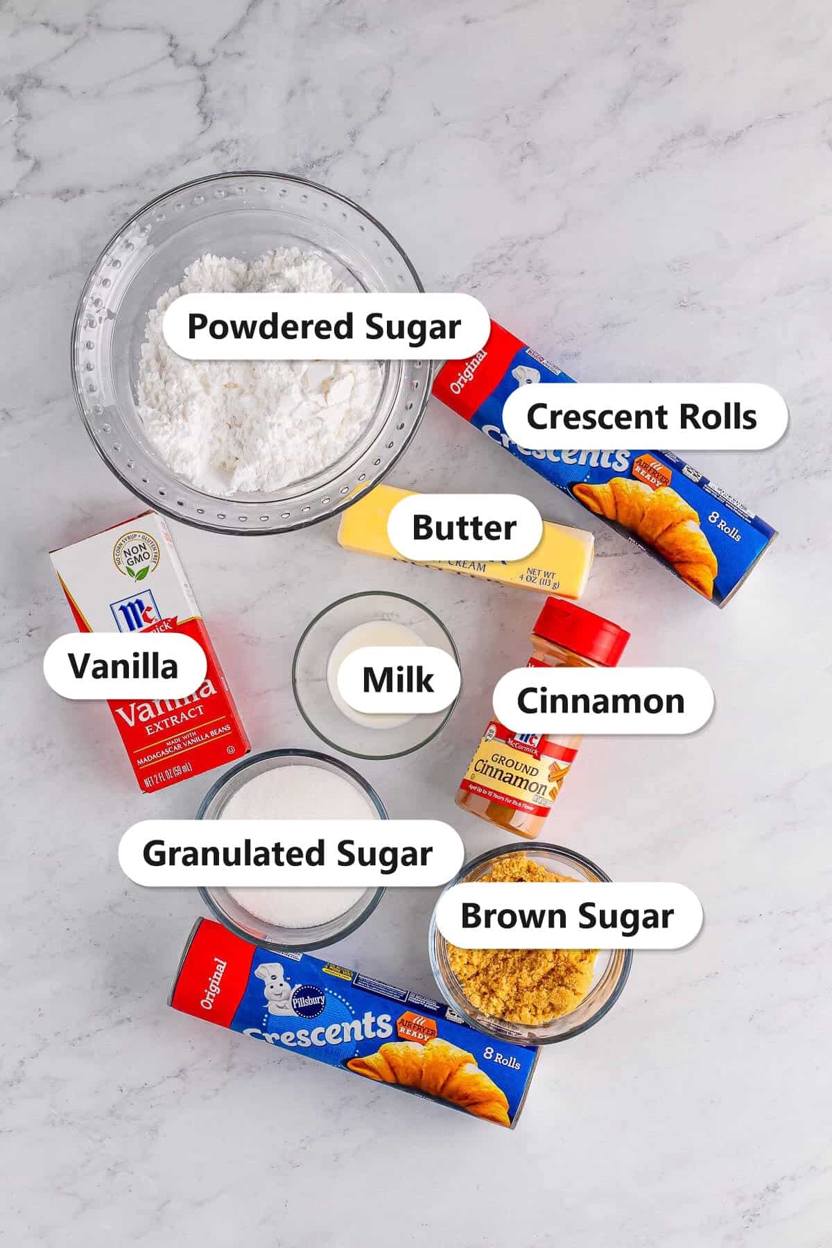 Labeled ingredients for crescent roll cinnamon rolls including powdered sugar, crescent rolls, butter, vanilla, milk, cinnamon, granulated sugar, and brown sugar.