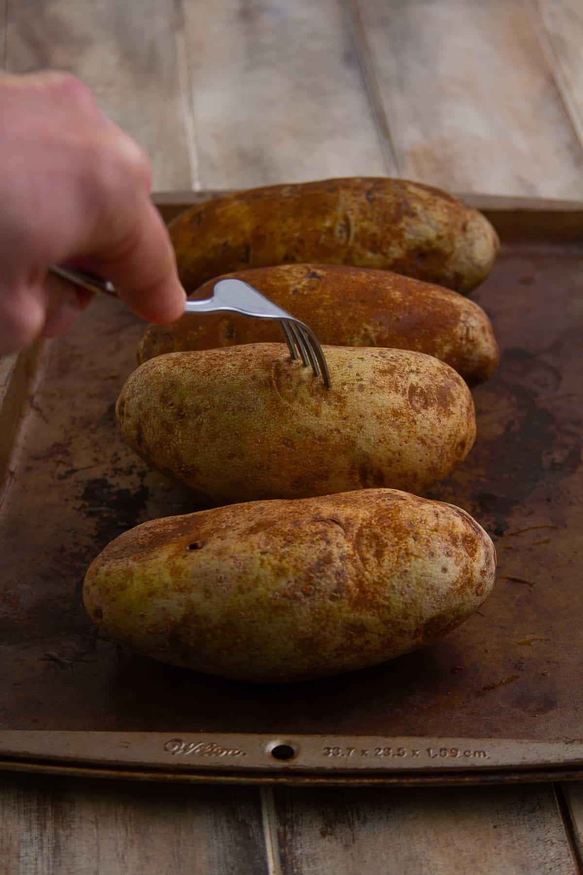 Hand poking a russet potato with a fork to let steam escape during baking for Crispy Baked Potato.