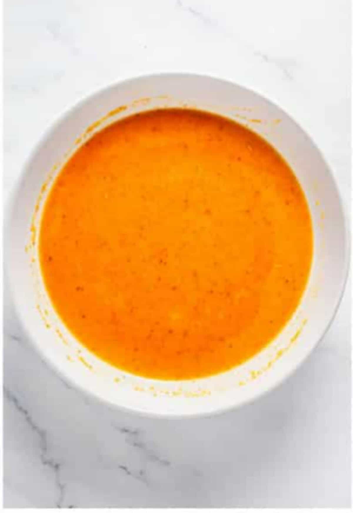 Whisking eggs water and buffalo sauce together in a bowl while oil heats in a Dutch oven for Crispy Southern Fried Chicken.