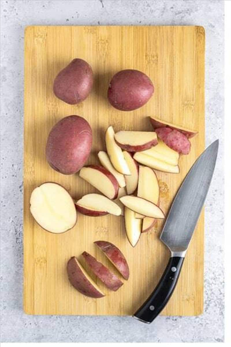 Red potatoes cut into wedges on a wooden cutting board for Deep Fried Potato Wedges.