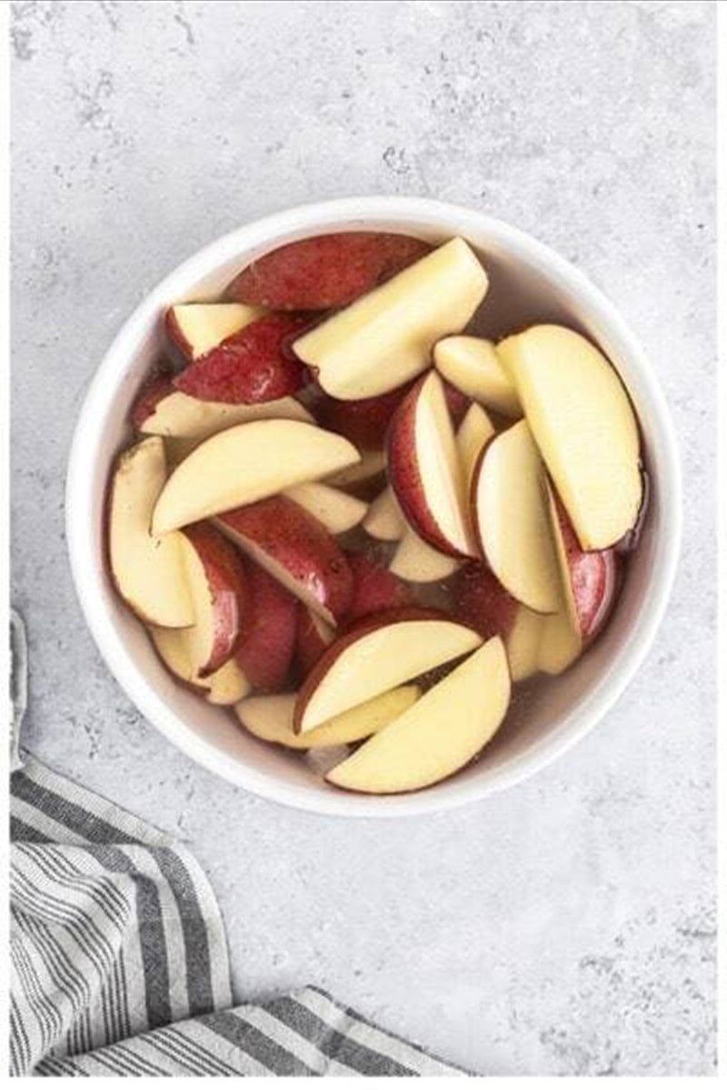 Red potato wedges soaking in cold water in a white bowl for Deep Fried Potato Wedges.