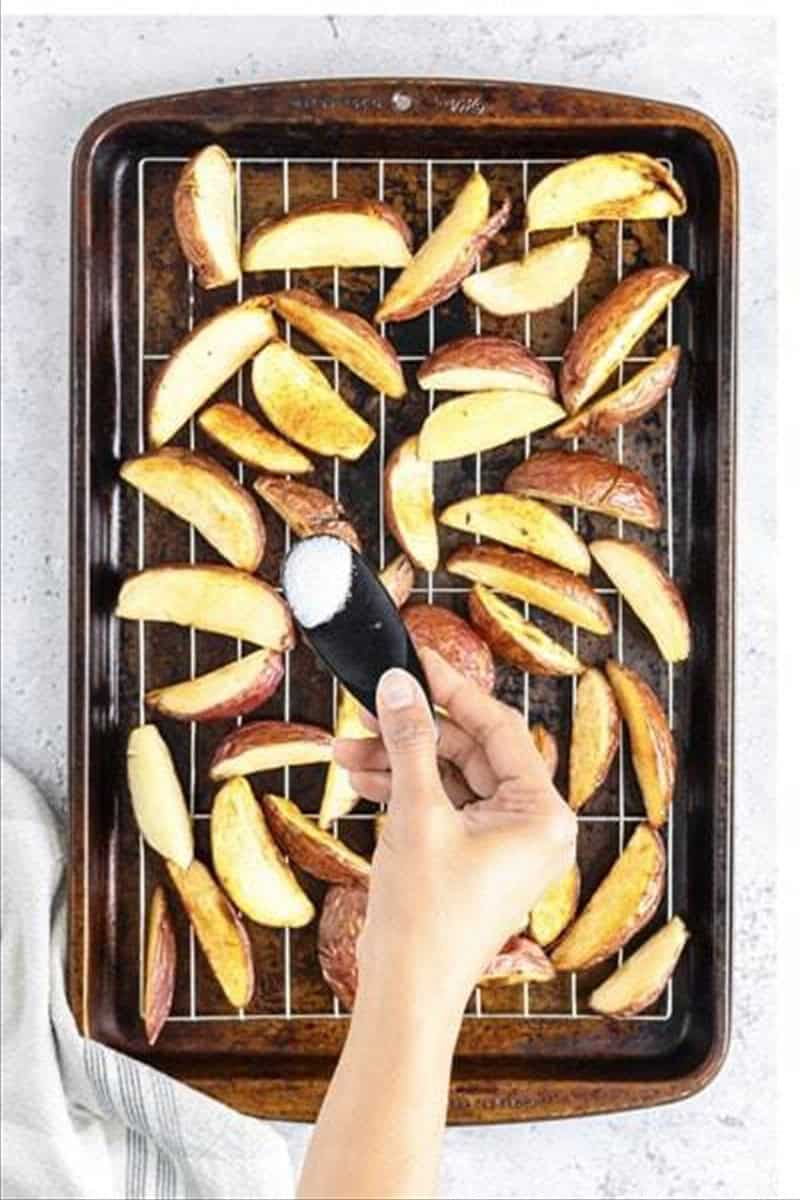 Pale parboiled potato wedges draining on a wire rack after the first fry for Deep Fried Potato Wedges.