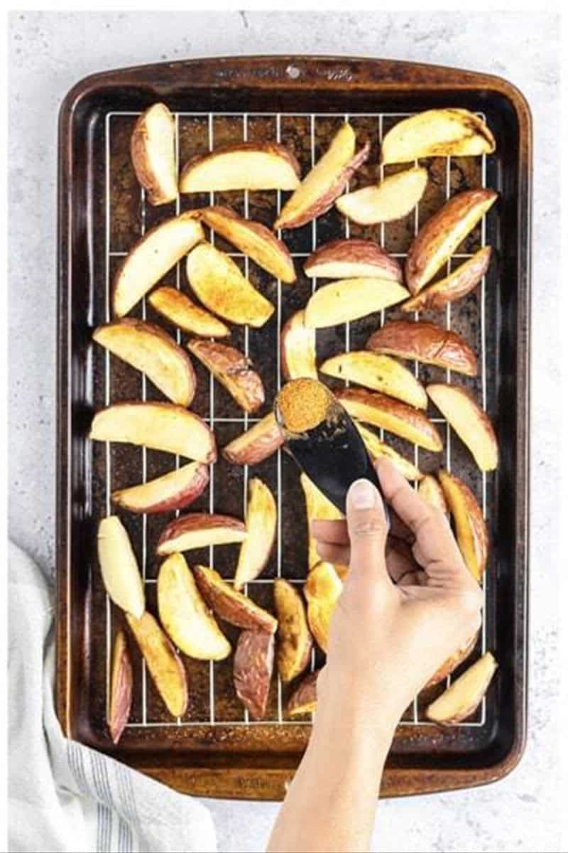 Hand sprinkling season salt over Deep Fried Potato Wedges fresh from the fryer.