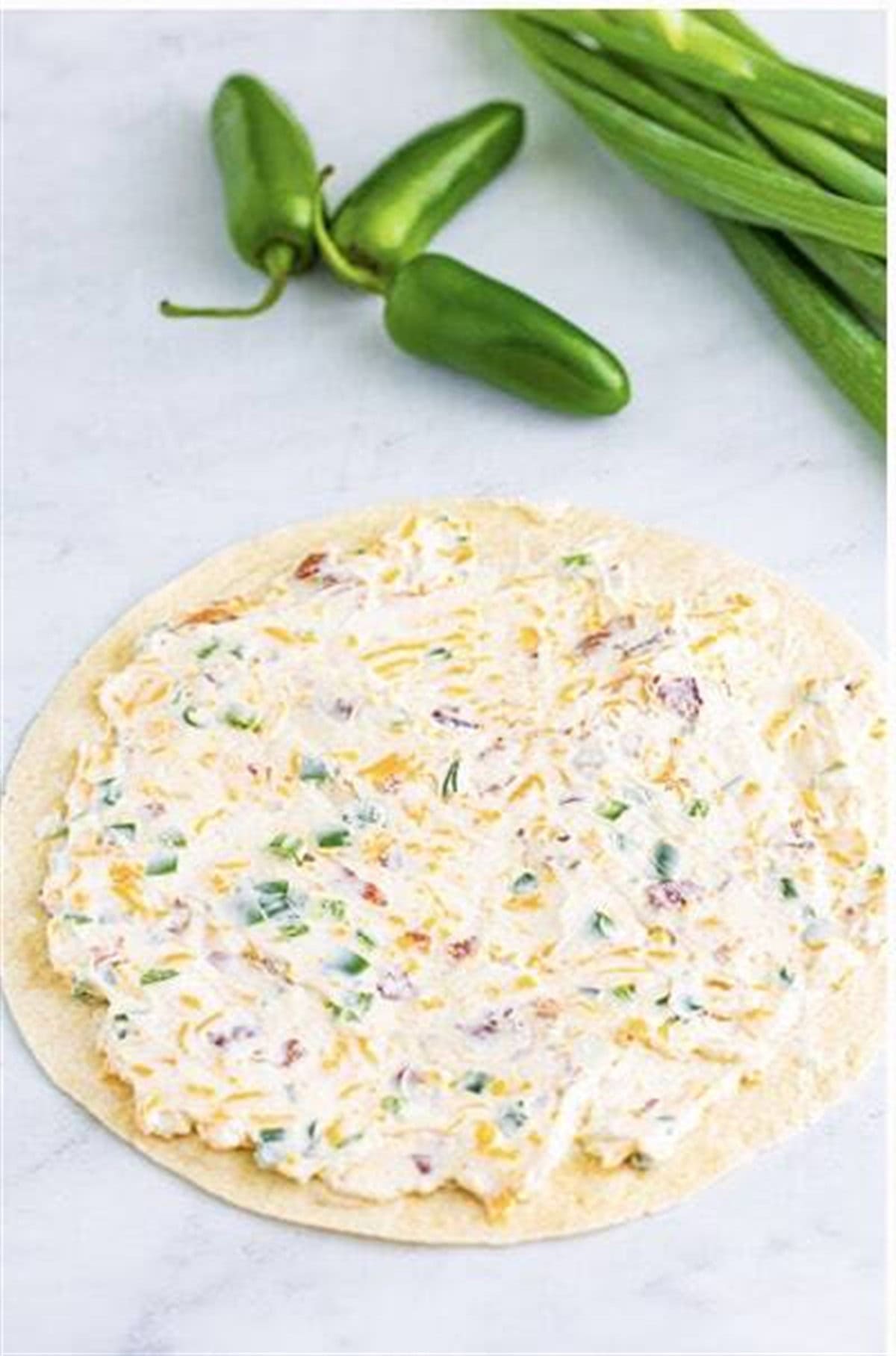 Jalapeno popper cream cheese filling spread evenly on a flour tortilla for Easy Cream Cheese Pinwheels.