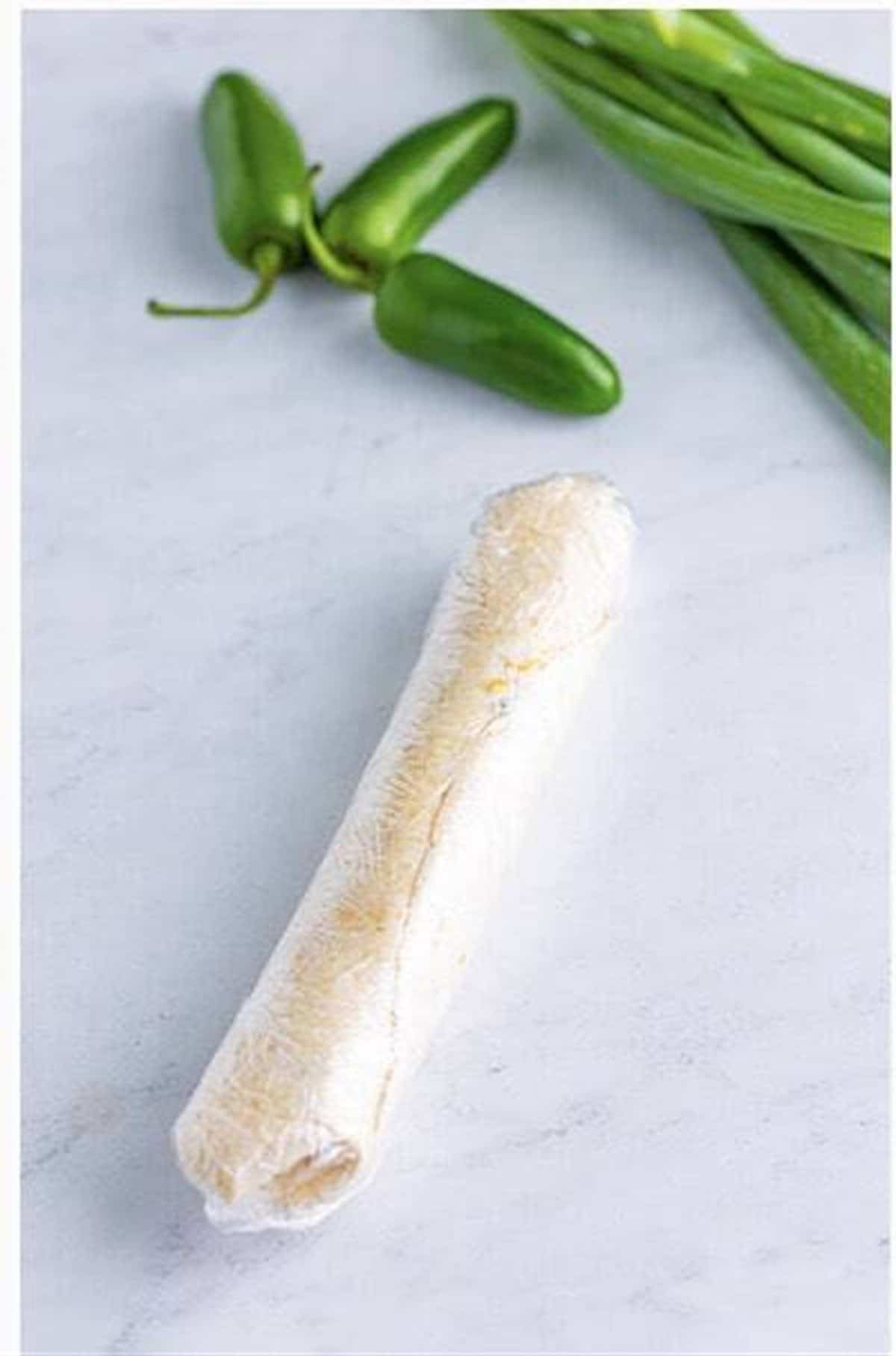 Tortilla rolled tightly into a log around cream cheese filling for Easy Cream Cheese Pinwheels (Jalapeno Popper).