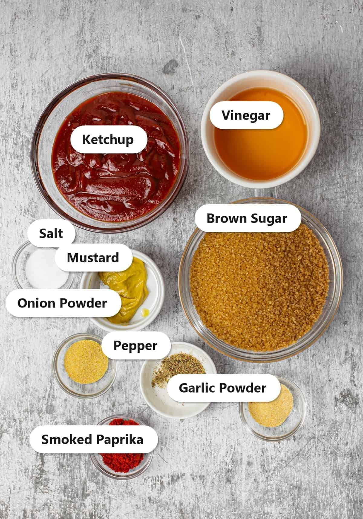 Labeled ingredients for Easy Homemade BBQ Sauce Recipe showing ketchup, brown sugar, apple cider vinegar, yellow mustard, smoked paprika, onion powder, garlic powder, kosher salt, and black pepper.