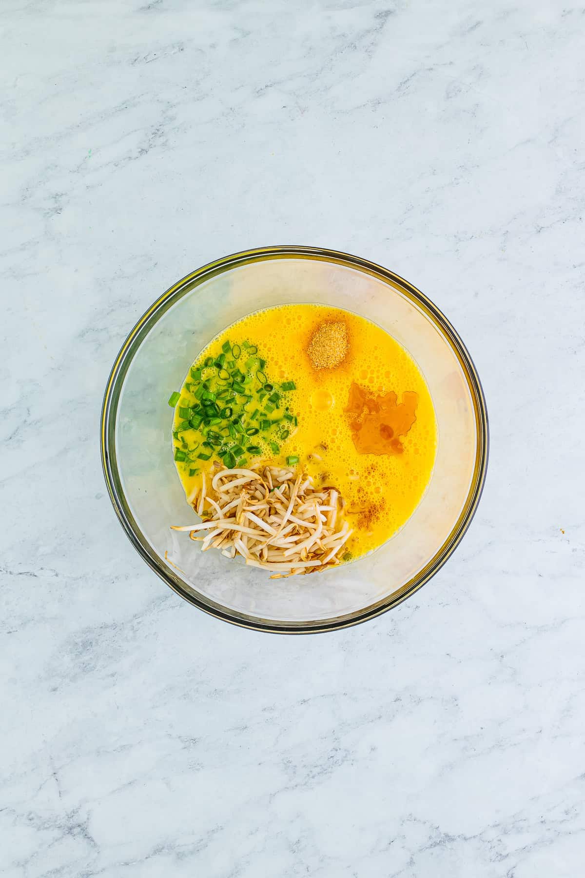 Beaten eggs combined with bean sprouts, green onions, and seasonings in a glass bowl for egg foo young.