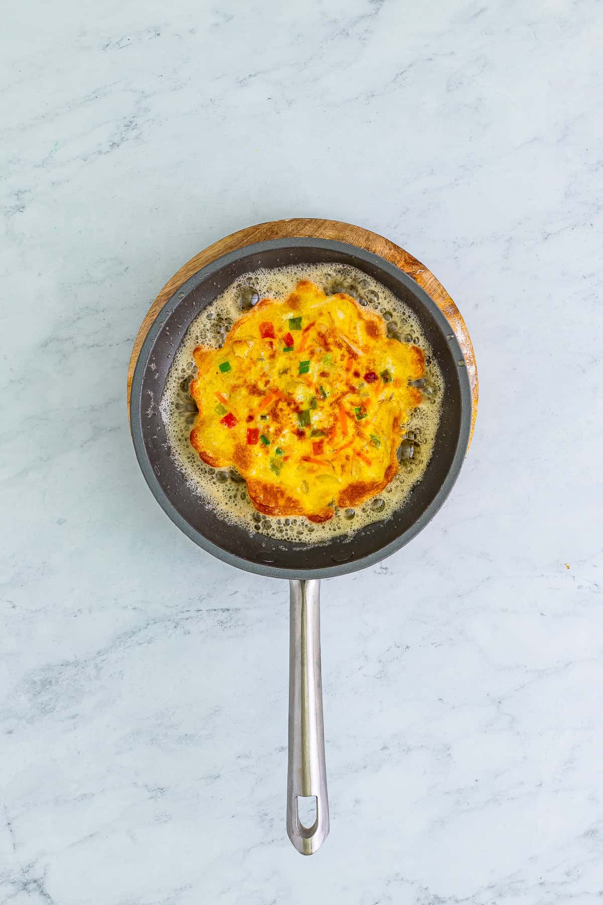 An egg foo young patty frying to golden brown in a skillet.