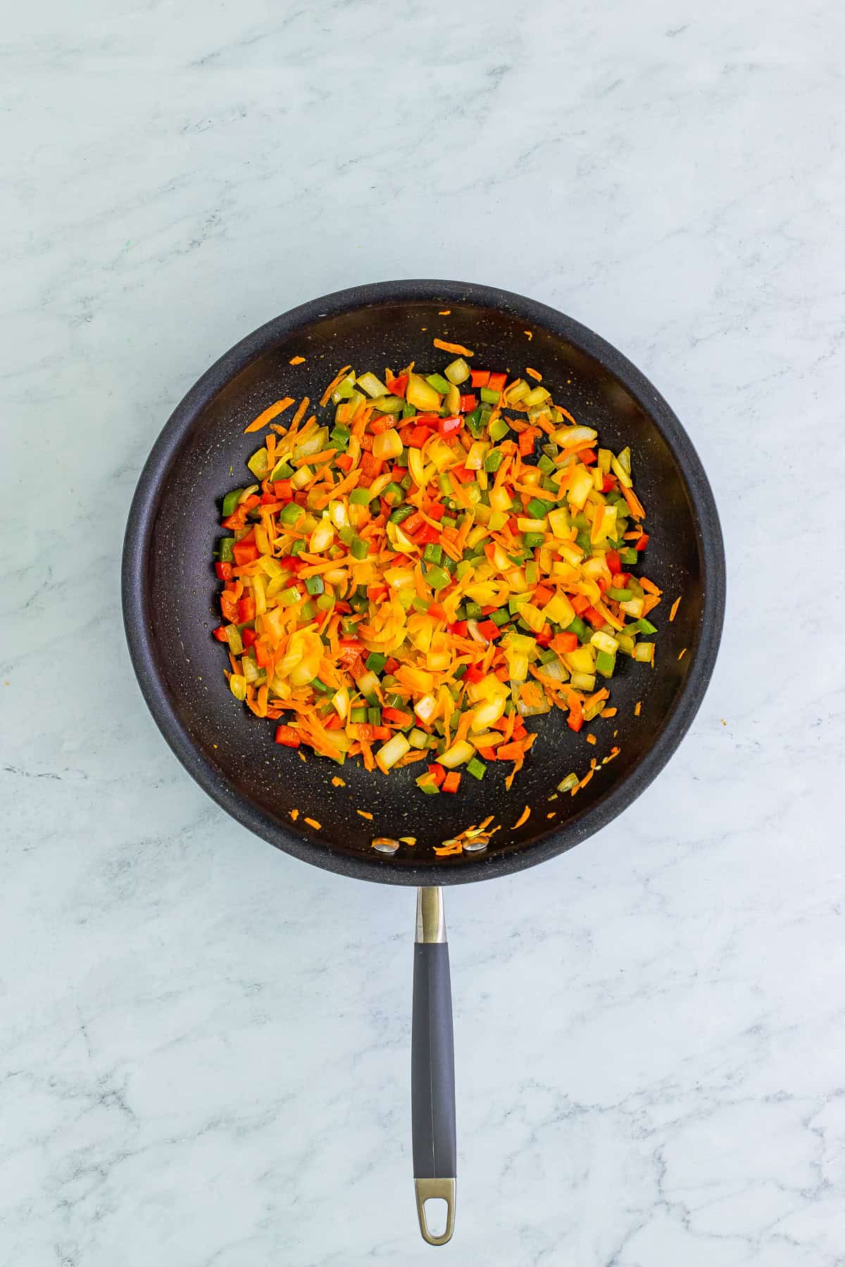 Diced bell peppers, onion, and shredded carrot cooking in a skillet for egg foo young.