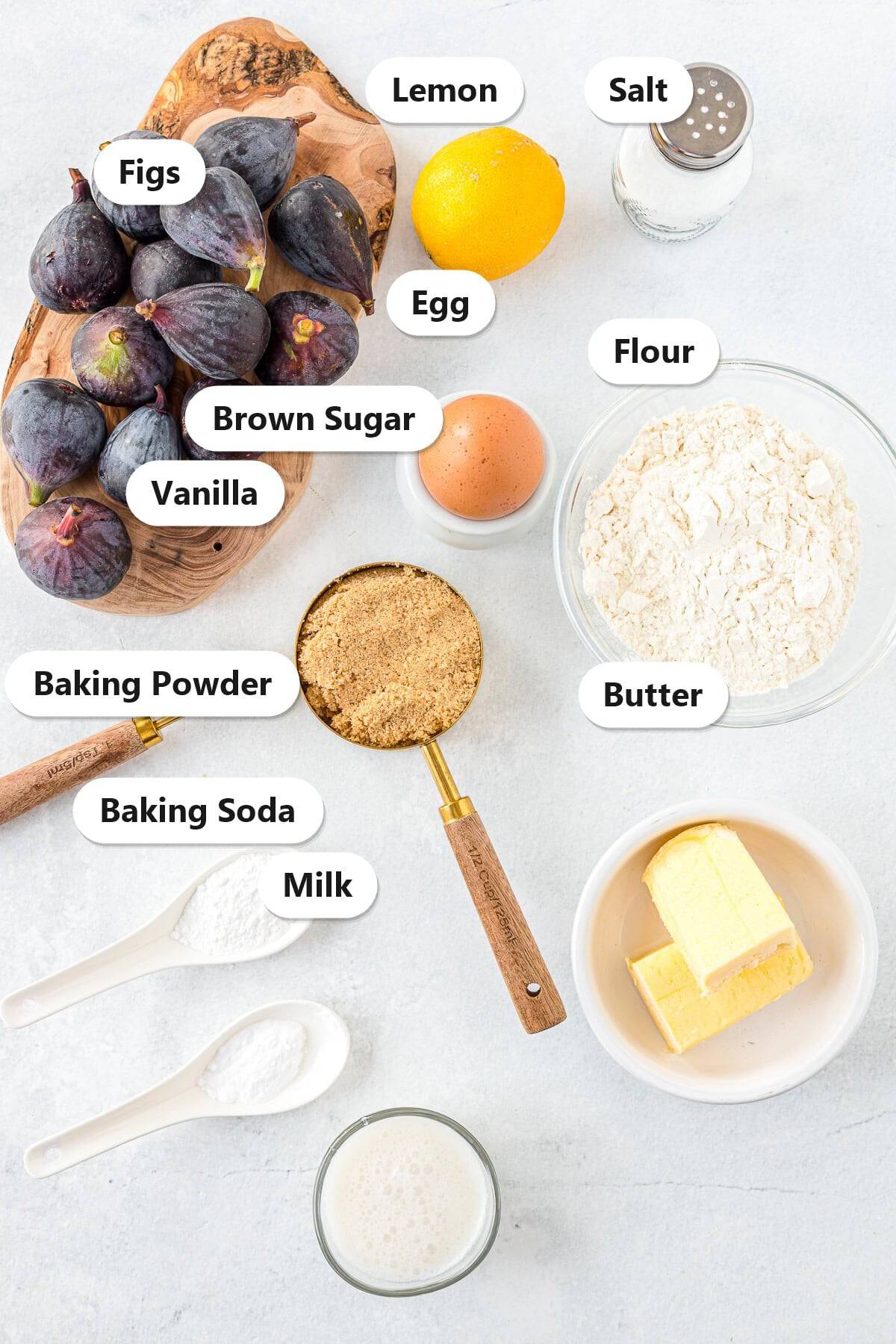 Labeled ingredients to make fig newton recipe including fresh figs, lemon, brown sugar, flour, butter, egg, milk, vanilla, and leaveners.