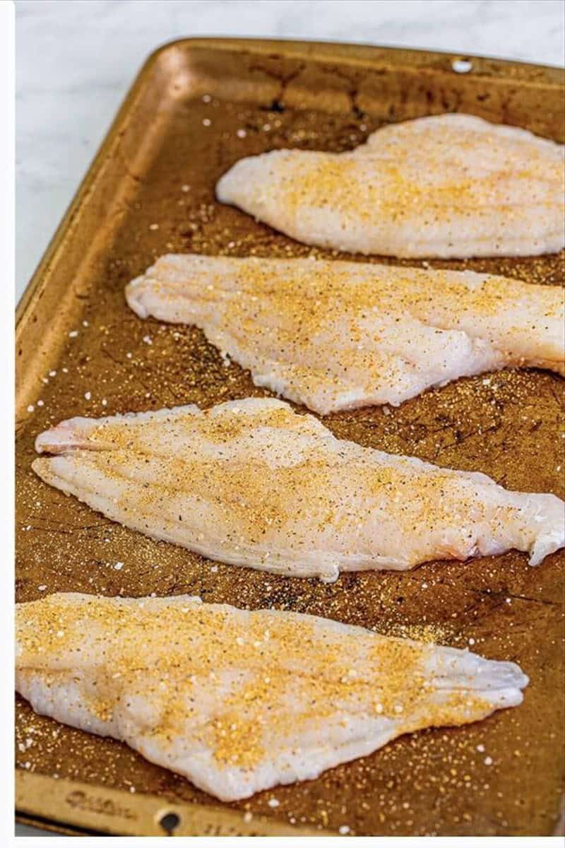 Raw catfish filets seasoned with Old Bay and spices on a sheet tray for fried catfish recipe.