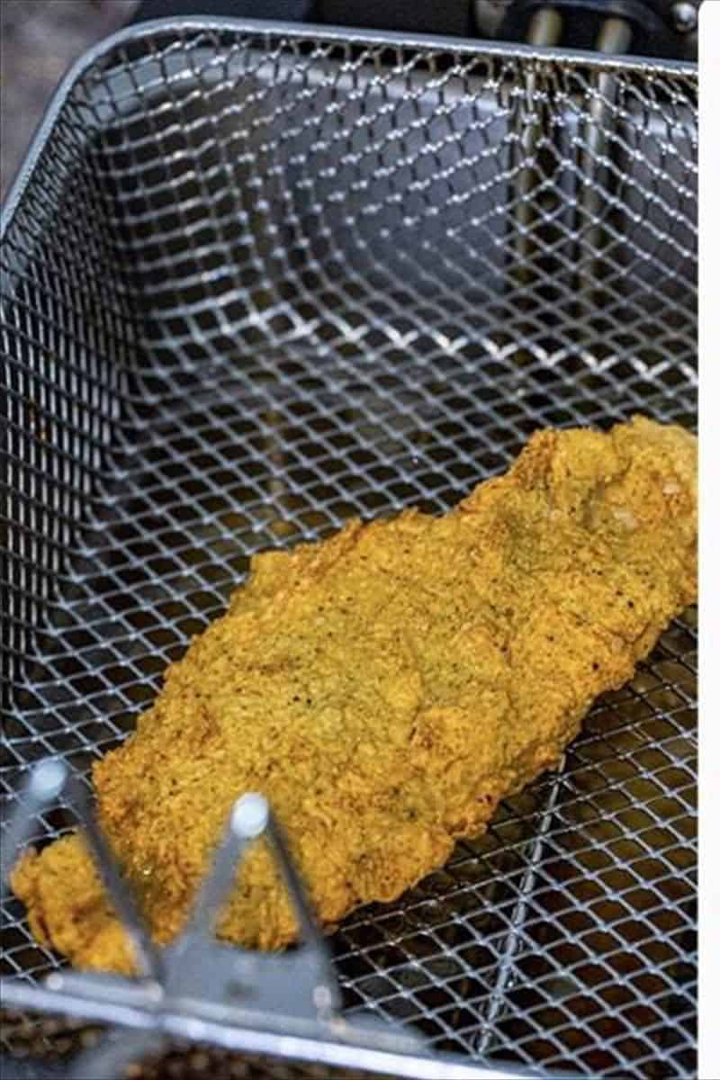 Catfish filet frying in hot oil in a deep fryer basket for fried catfish recipe.