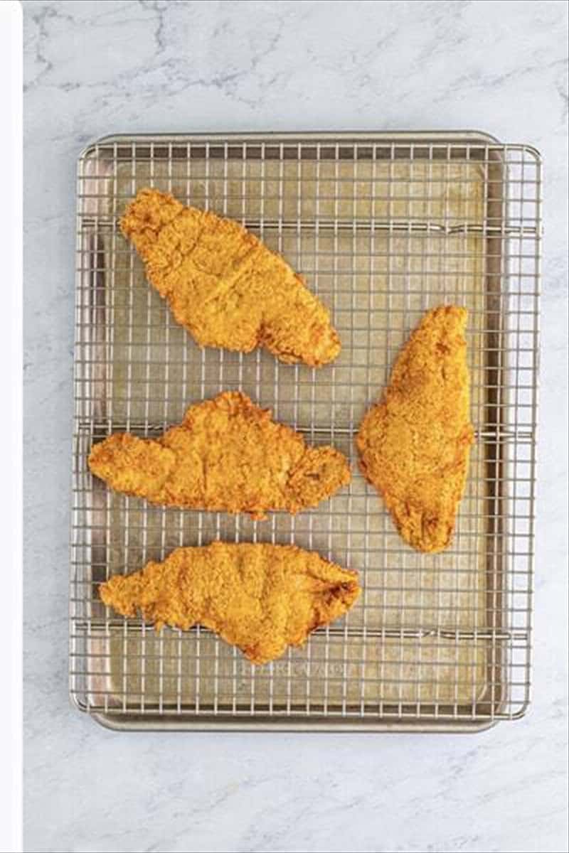 Golden fried catfish filets draining on a wire cooling rack after deep frying.