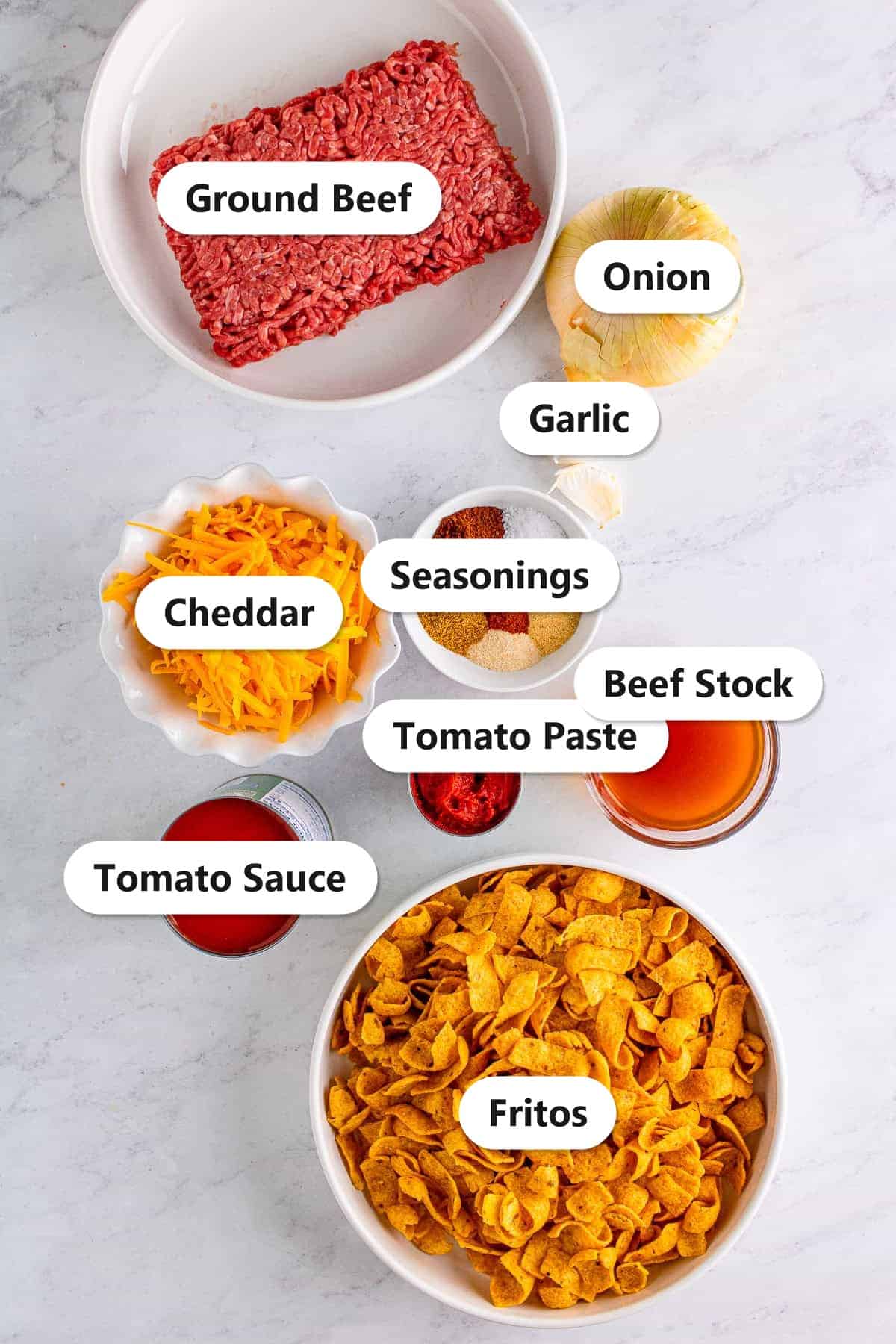 Labeled ingredients for Frito pie casserole including ground beef, Fritos, cheddar cheese, tomato sauce, and chili seasonings.