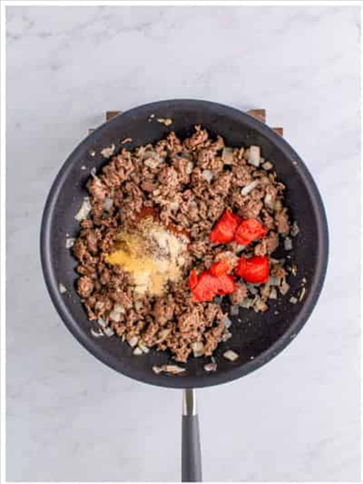 Ground beef browning with onion, chili seasonings, and tomato paste in a skillet for Frito pie casserole.
