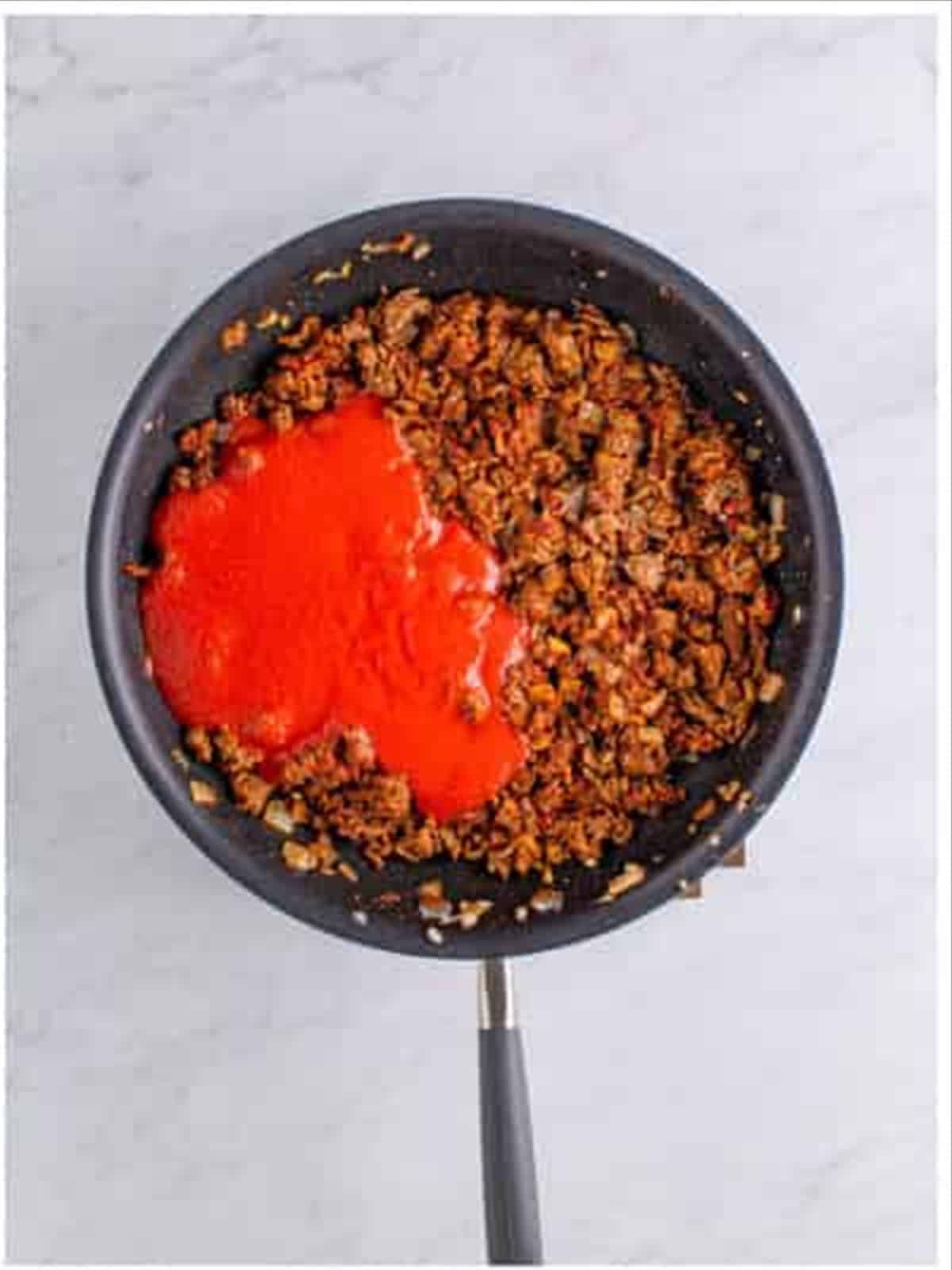 Tomato sauce and beef stock stirred into the seasoned beef to build the chili.