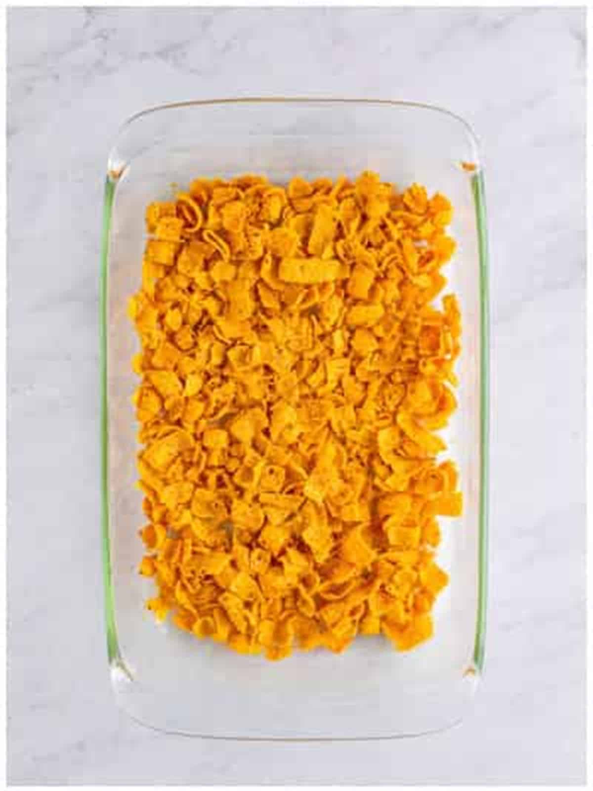 A layer of crushed Fritos spread in the bottom of a greased baking dish.