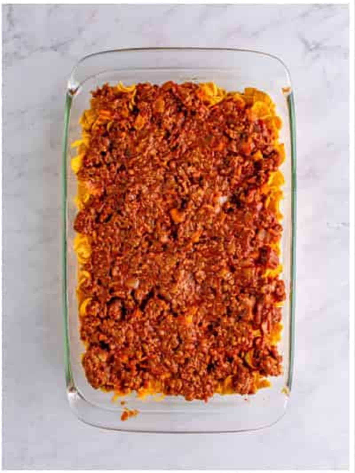 Half of the chili spooned over the Fritos layer in the baking dish.