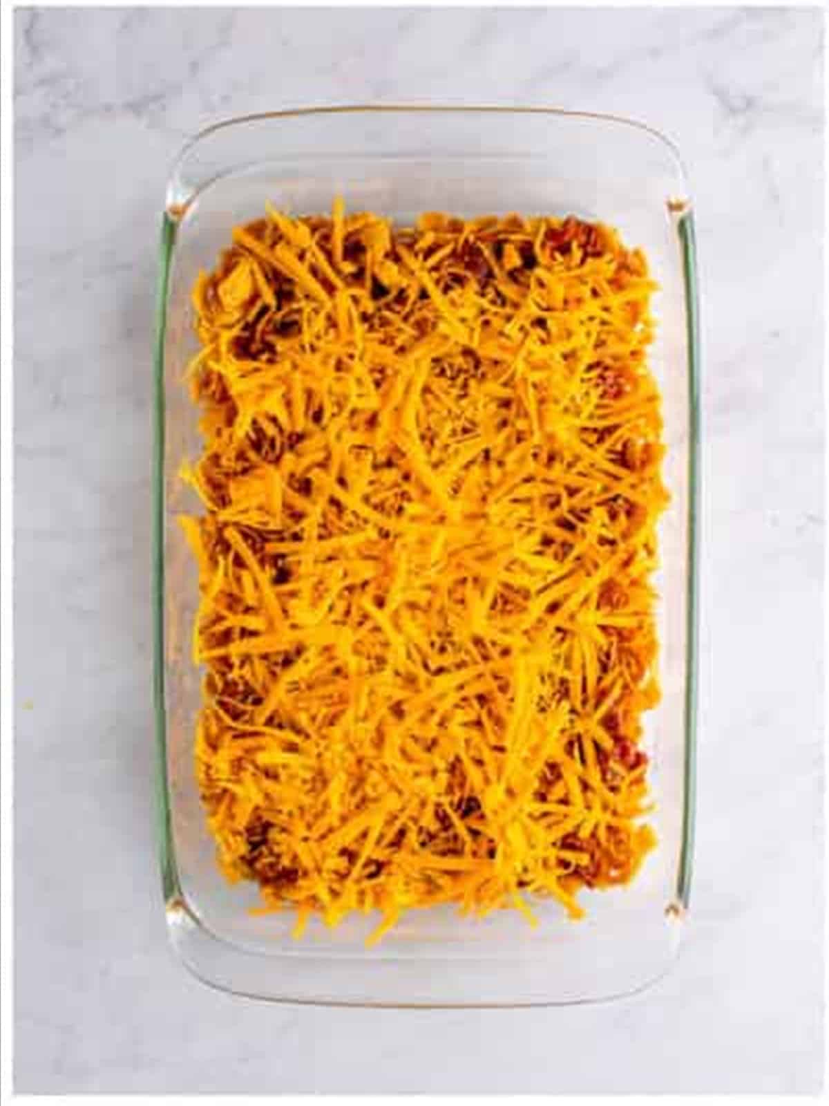 Shredded cheddar cheese layered over the chili in the Frito pie casserole.