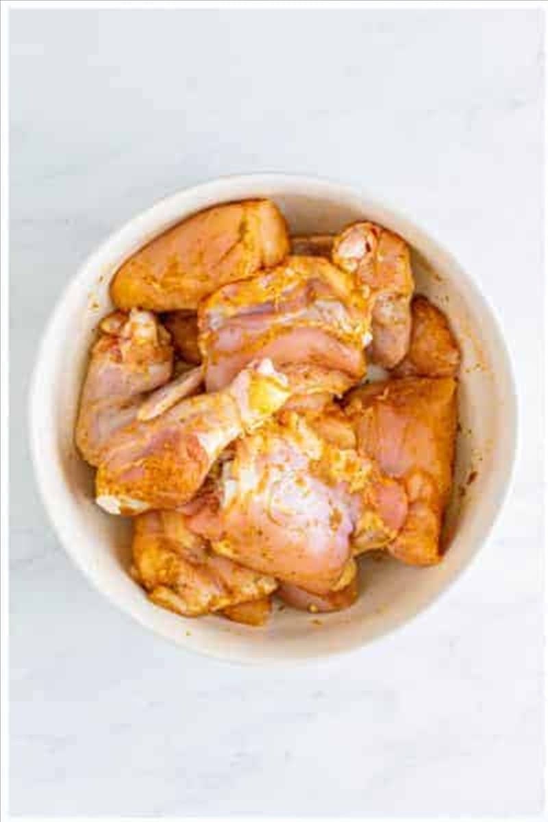 Raw chicken pieces tossed with garlic powder seasoned salt black pepper and onion powder in a large white bowl.