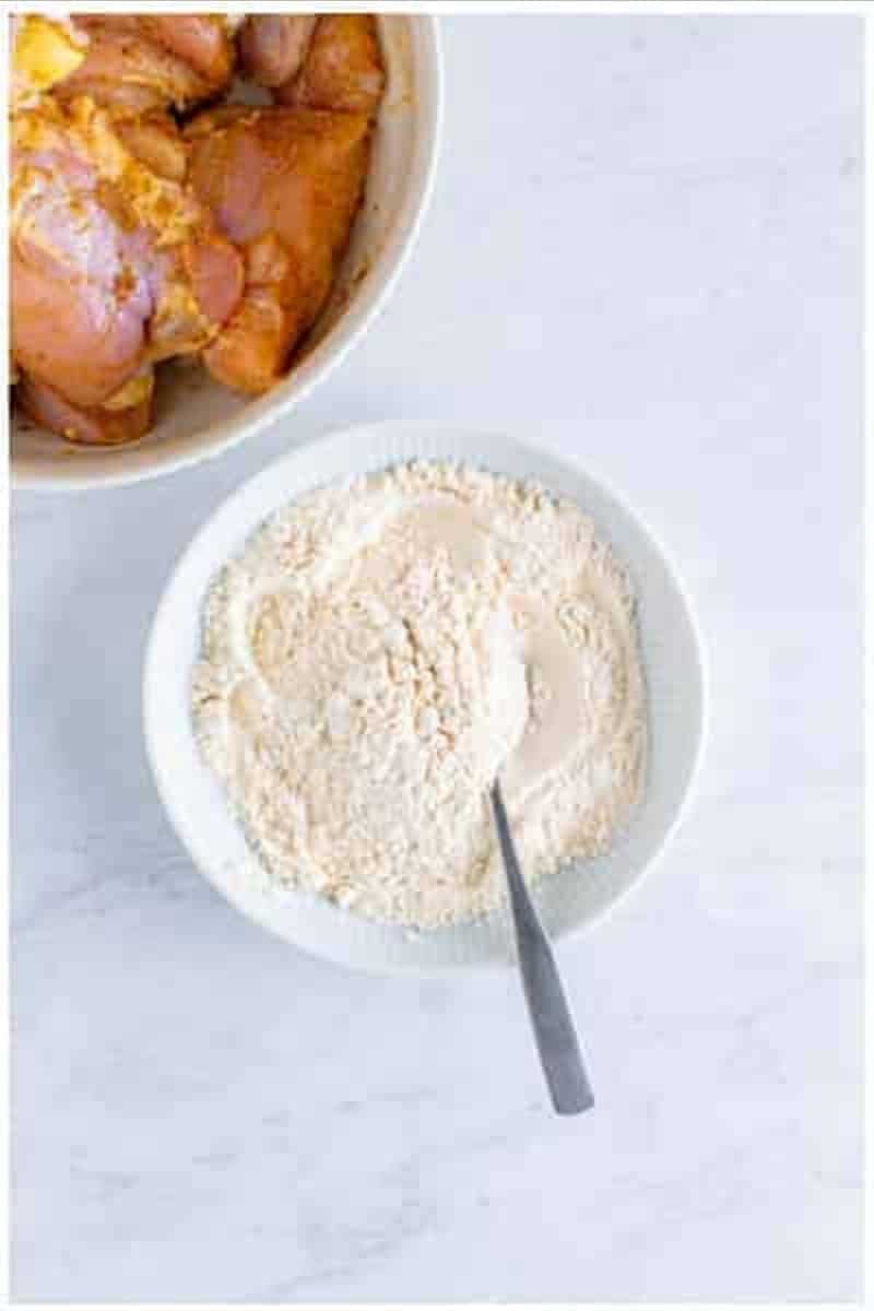 Small white bowl with all purpose flour baking powder and baking soda being stirred together with a spoon.
