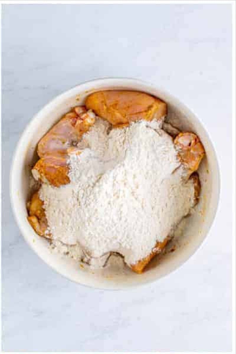 Flour mixture poured on top of the seasoned chicken pieces in the large bowl.