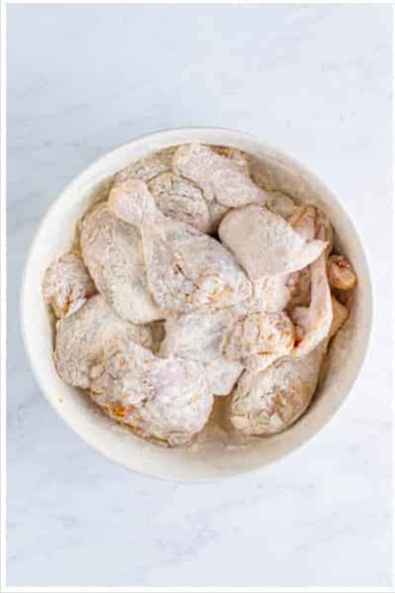 Chicken pieces tossed and coated with the dry flour mixture in the large white bowl.
