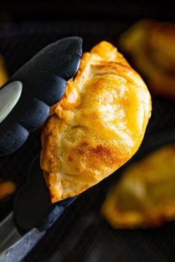 Golden crispy Trader Joe's pork gyoza in air fryer held with tongs after cooking.