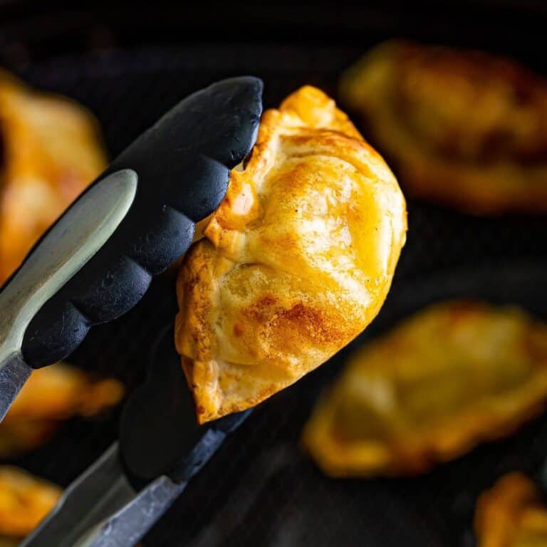 Golden crispy Trader Joe's pork gyoza in air fryer held with tongs after cooking.
