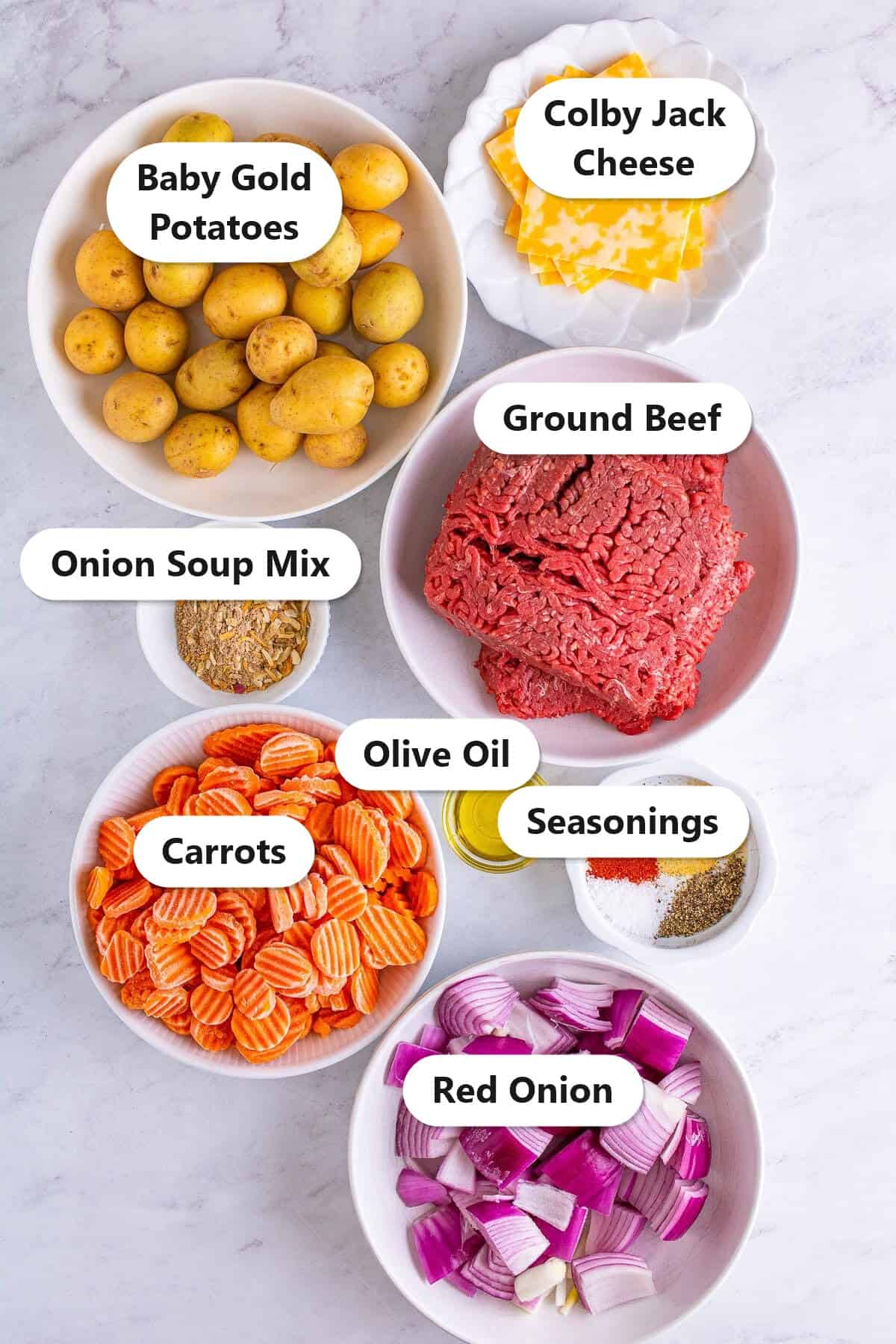 Labeled ingredients to make hamburger foil packets including ground beef, onion soup mix, baby gold potatoes, carrots, red onion, olive oil, seasonings, and Colby Jack cheese.