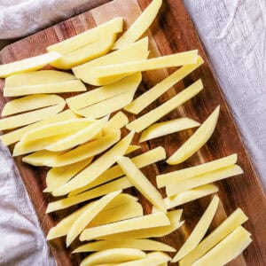 Preheating the oil in a deep fryer and cutting russet potatoes into Homemade French Fries sticks.